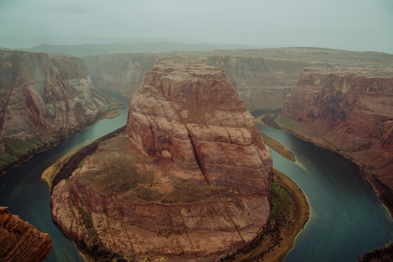 Aerial view of Horseshoe Bend, a dramatic red rock canyon curve of the Colorado River under overcast skies.