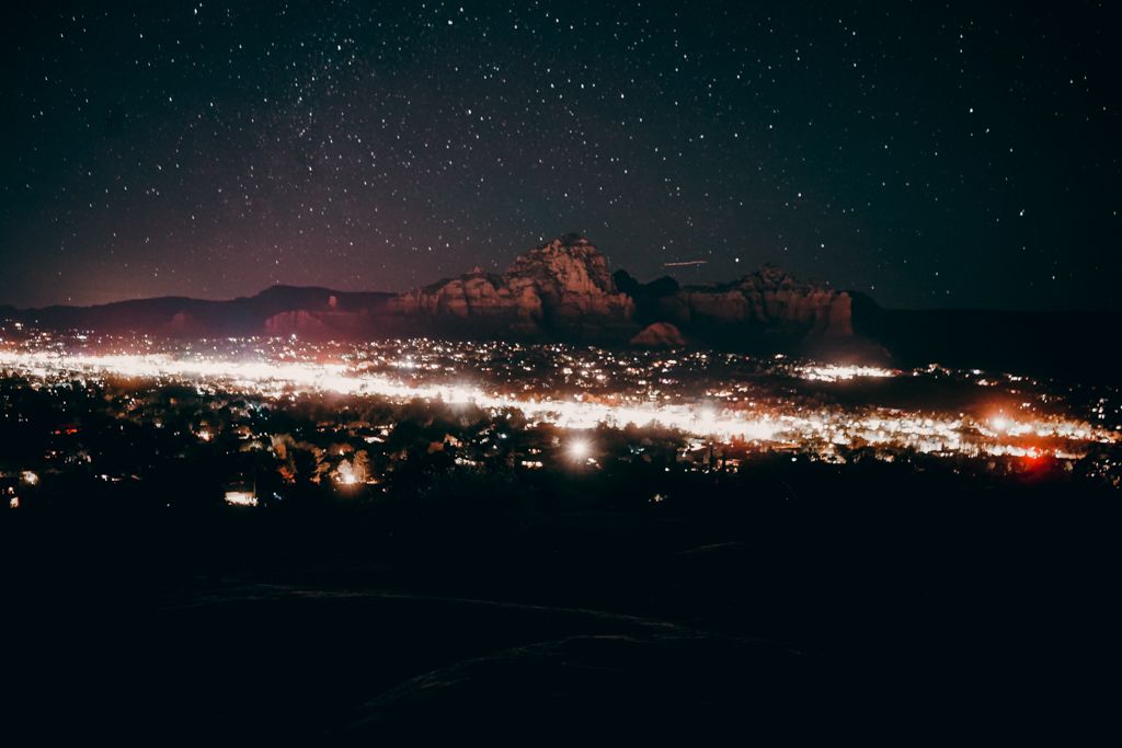 Stunning night sky filled with stars over a glowing desert town with red rock formations in the background.