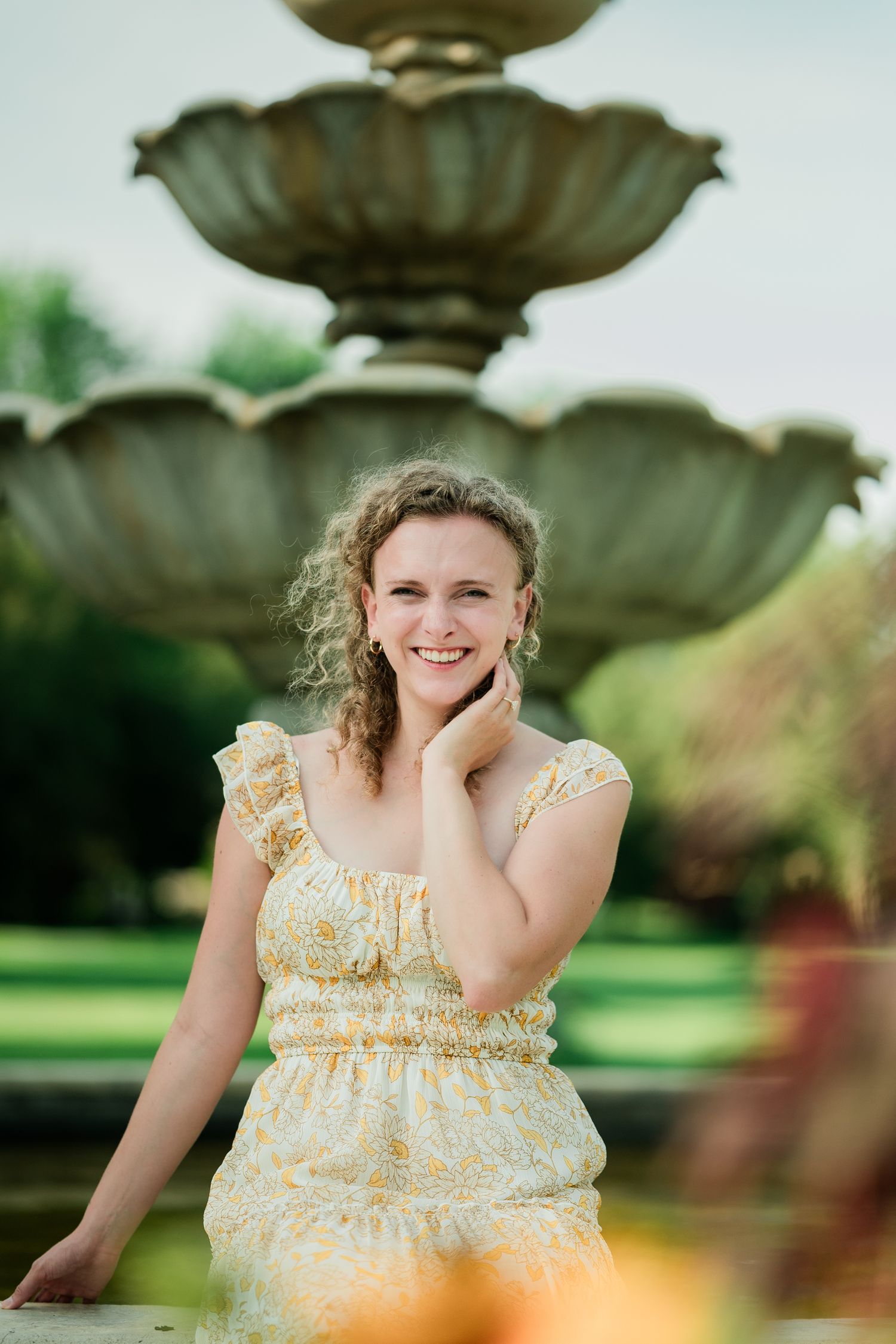 Emmy of Emmy Faye Photography smiling while sitting at a fountain at Arneson Acres in Edina, MN