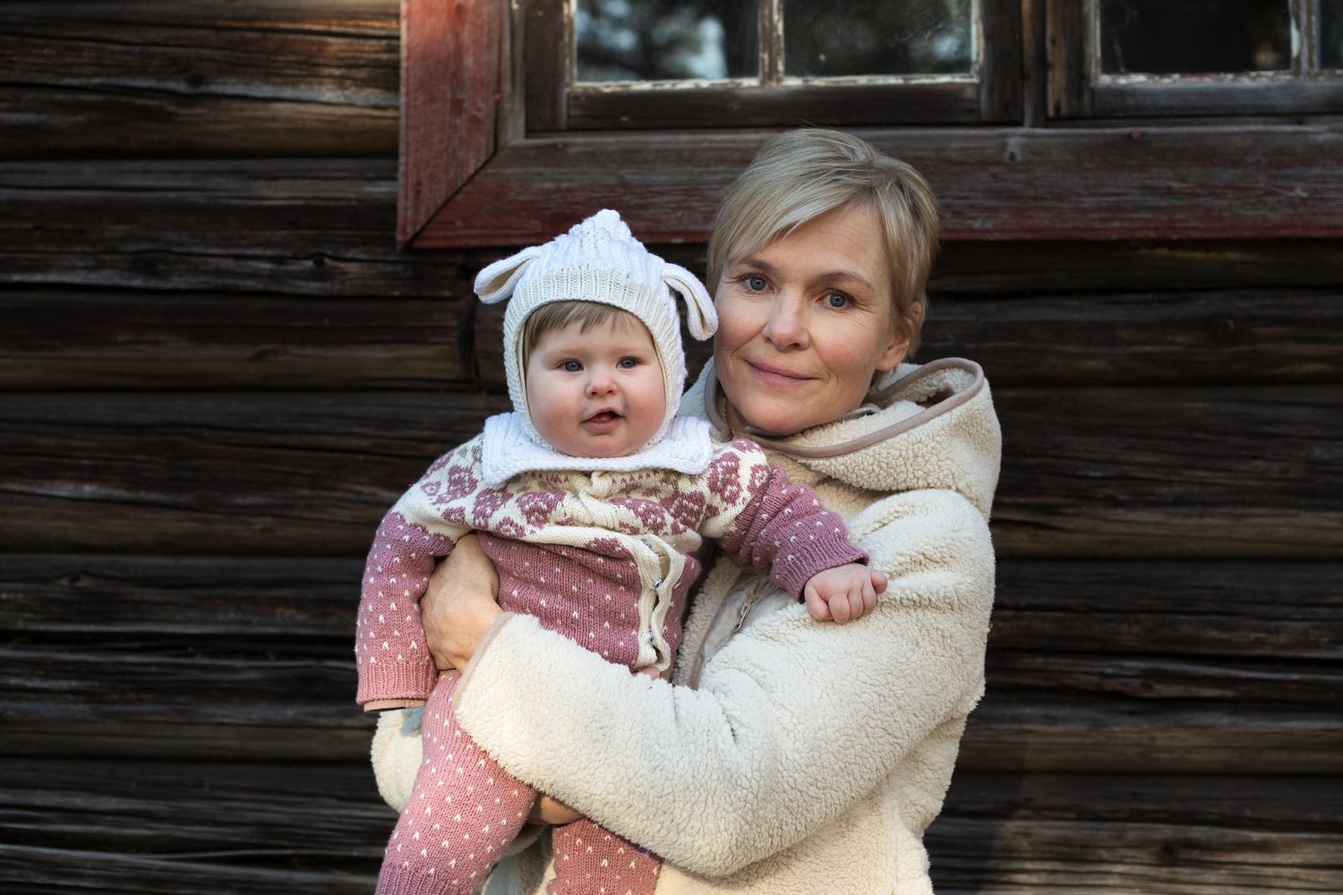 A cozy winter portrait against a rustic wooden cabin wall.