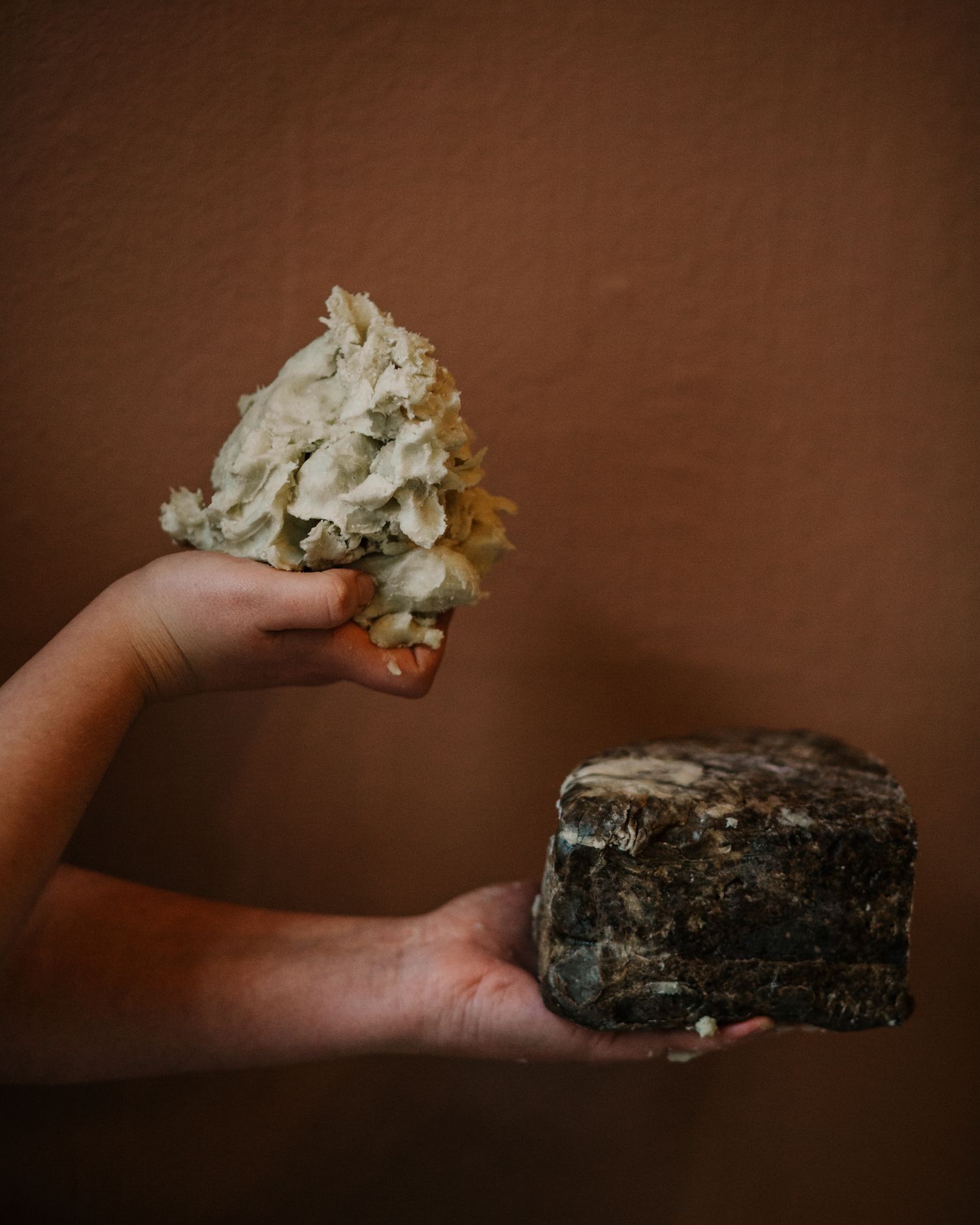 Hands holding contrasting light and dark mineral or stone specimens against a brown background.