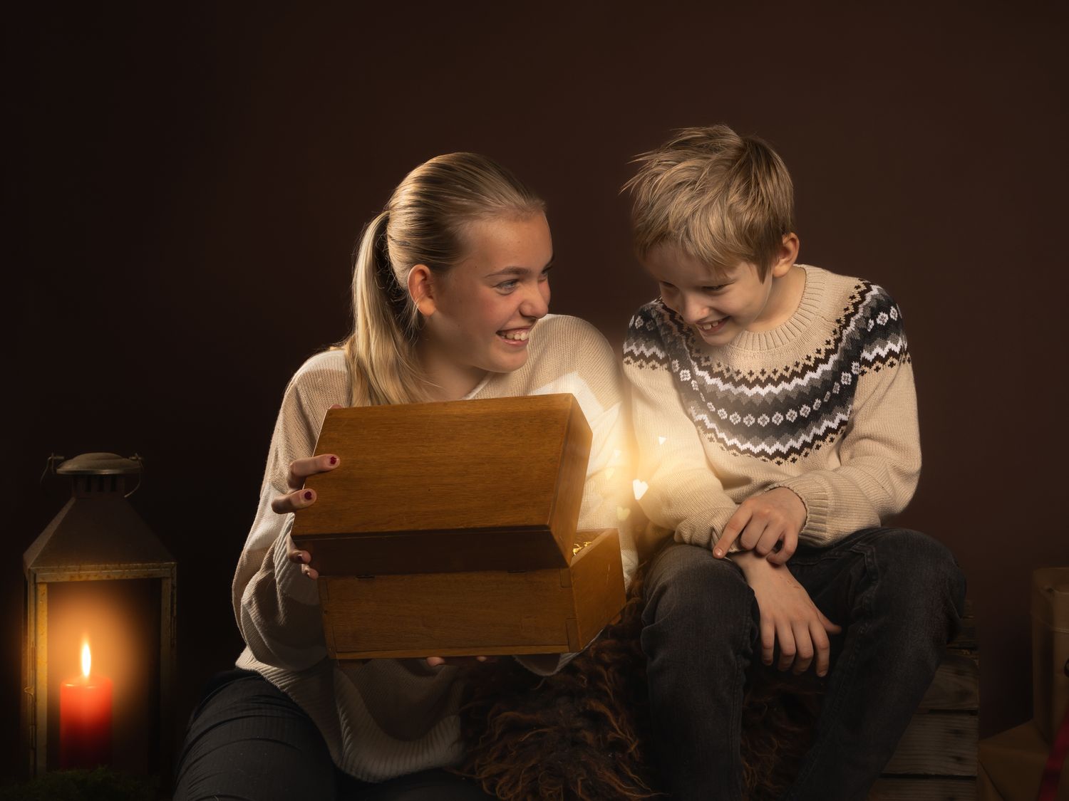 A candlelit scene shows two figures in winter sweaters leaning over a wooden box with warm glowing light.