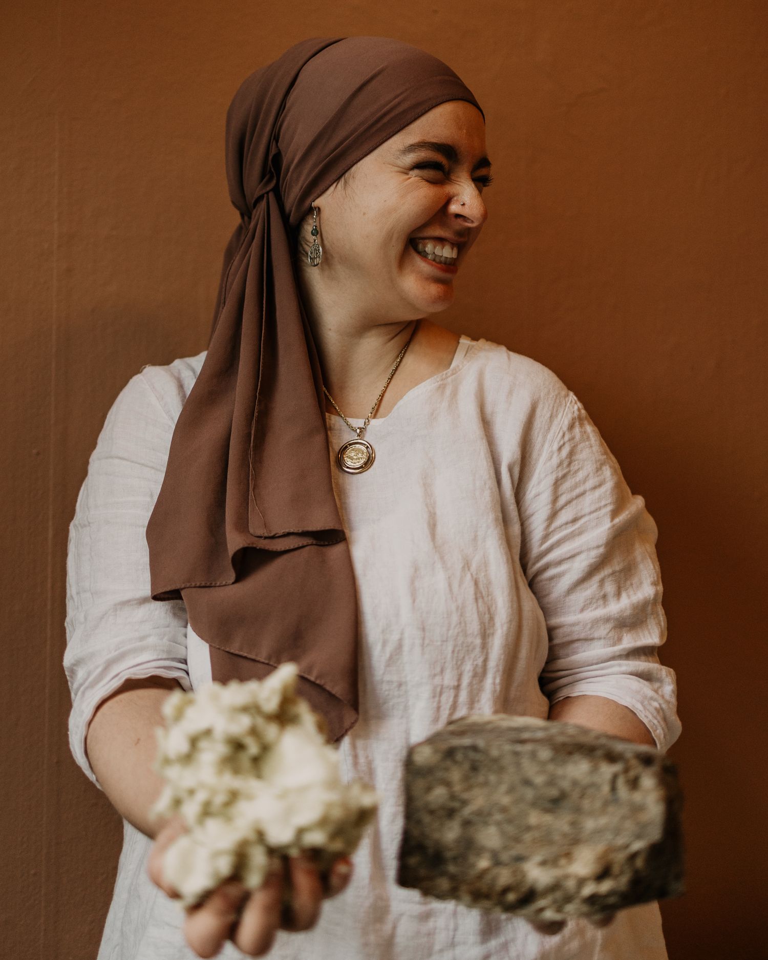 A person wearing a brown headscarf and white linen clothing displays mineral specimens.