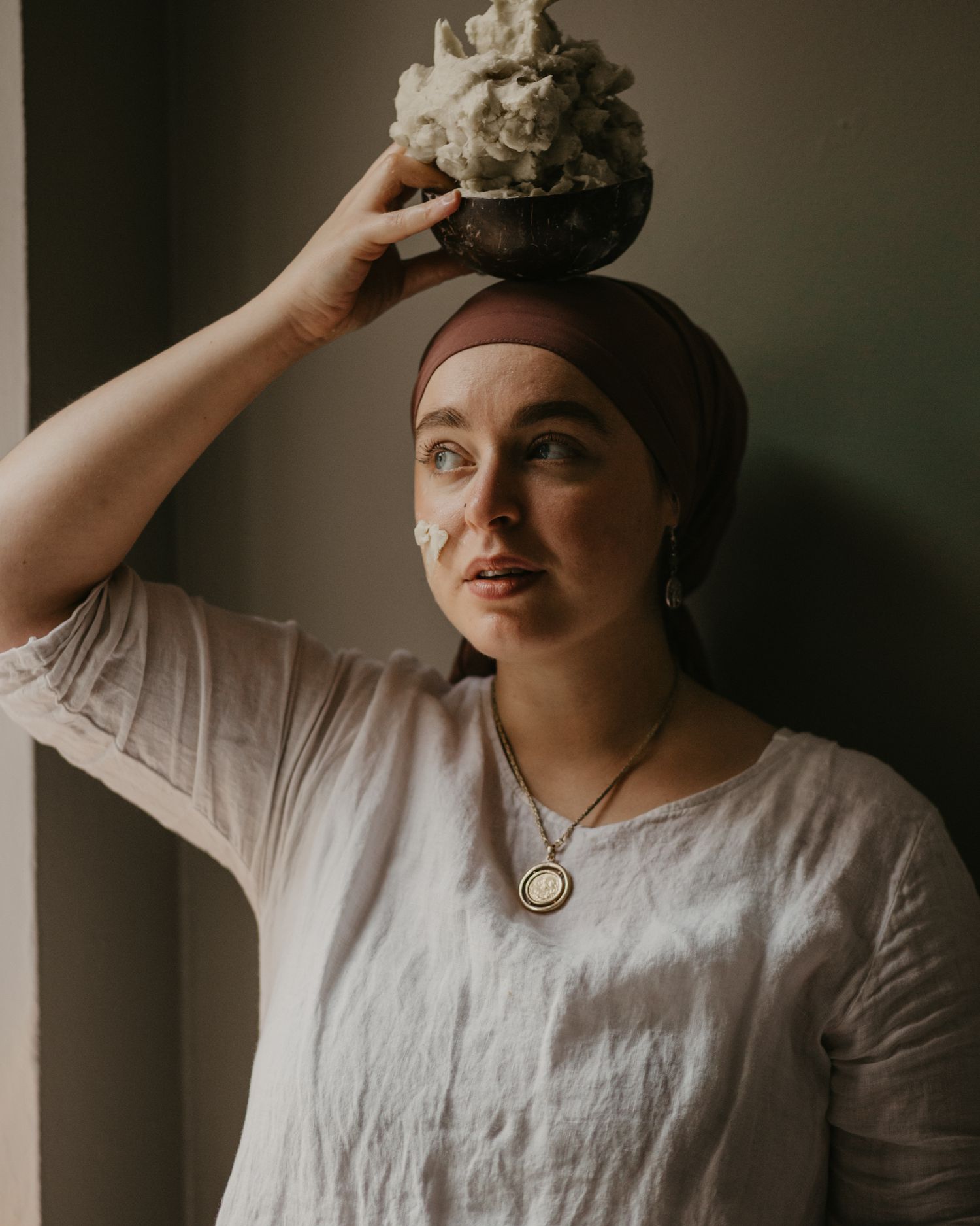 Person in white linen and headscarf holds a light-colored mineral specimen overhead.