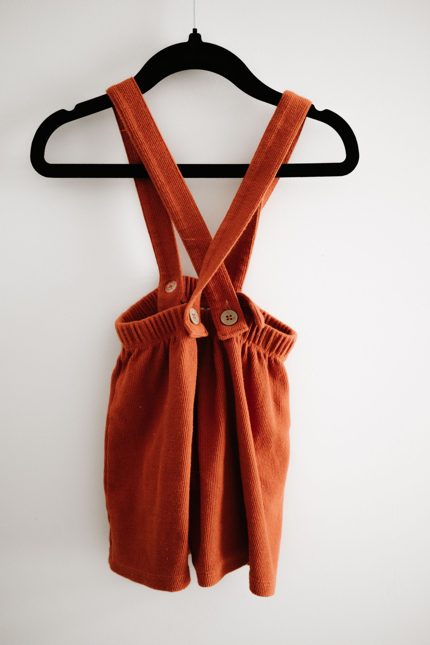 Burnt orange corduroy suspender shorts hanging on black velvet hanger.