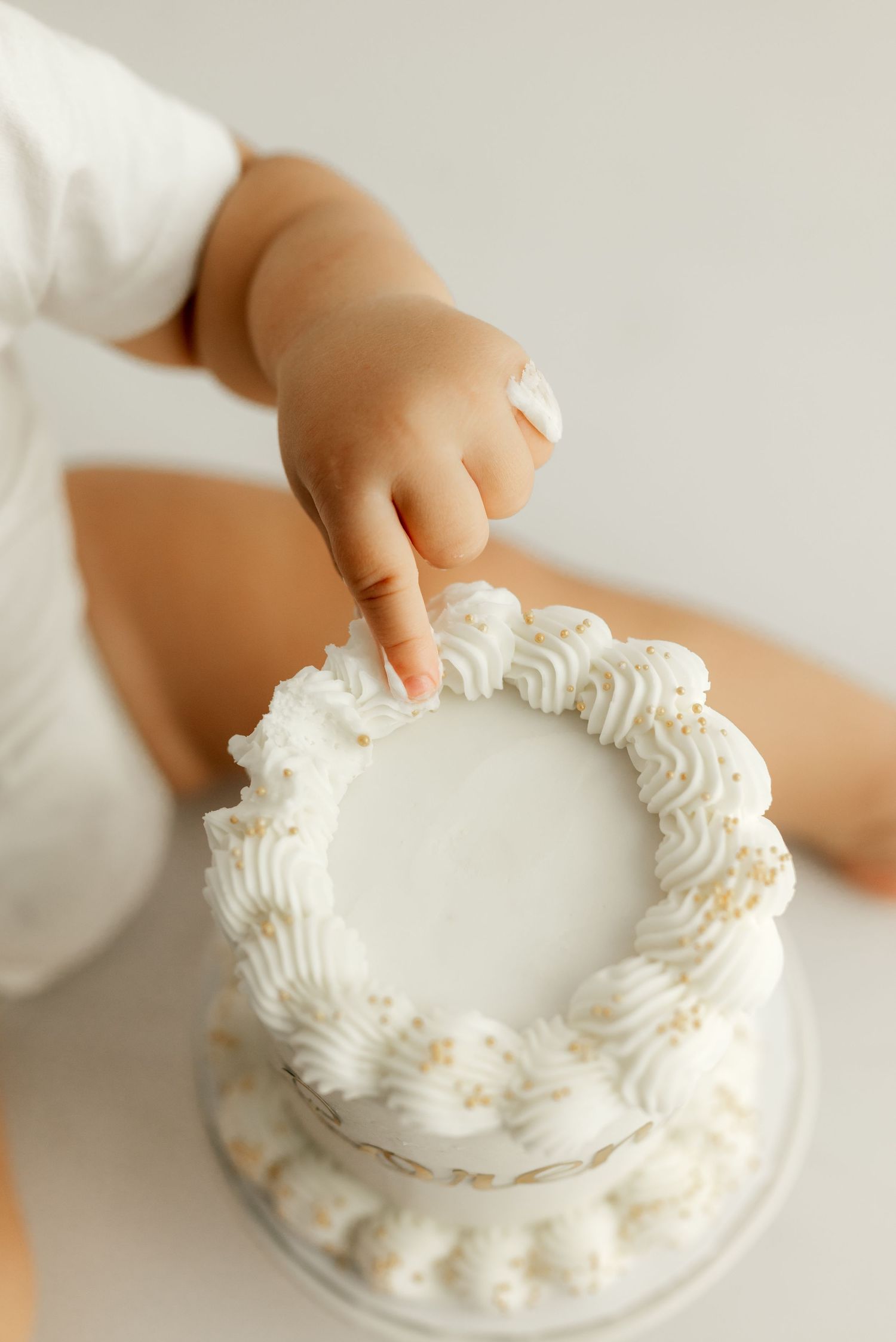 A small hand reaching to touch the white frosting on top of a cake.