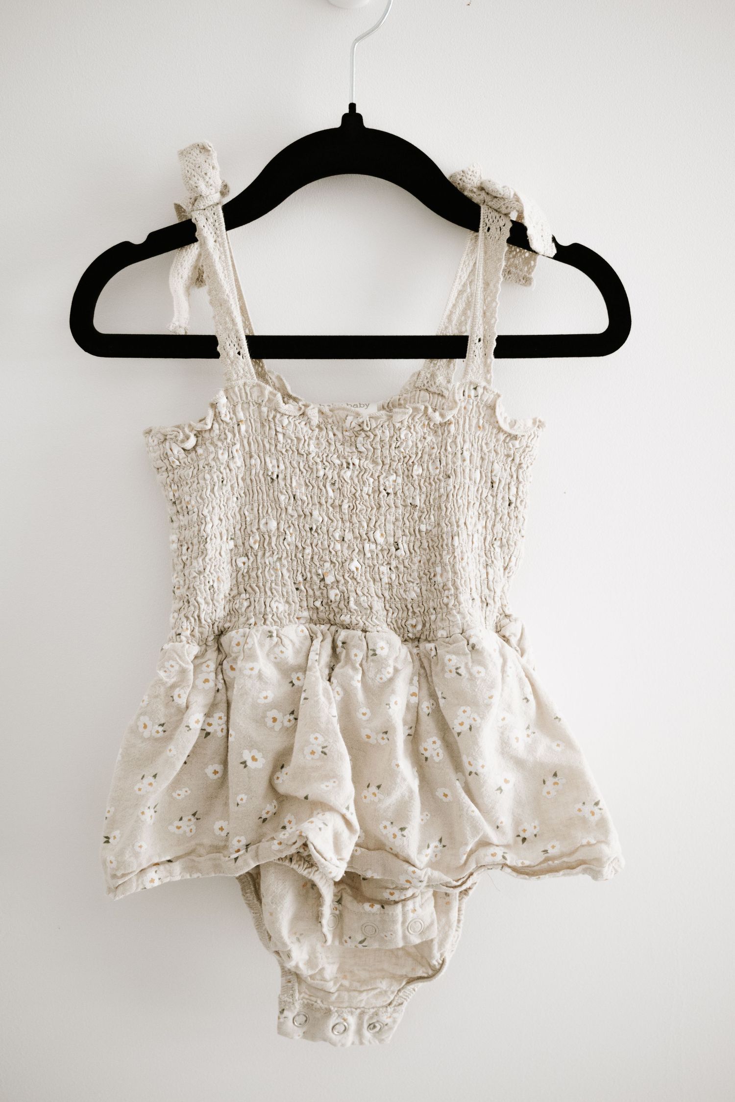Cream colored smocked baby romper with floral print and ruffle straps on black hanger.