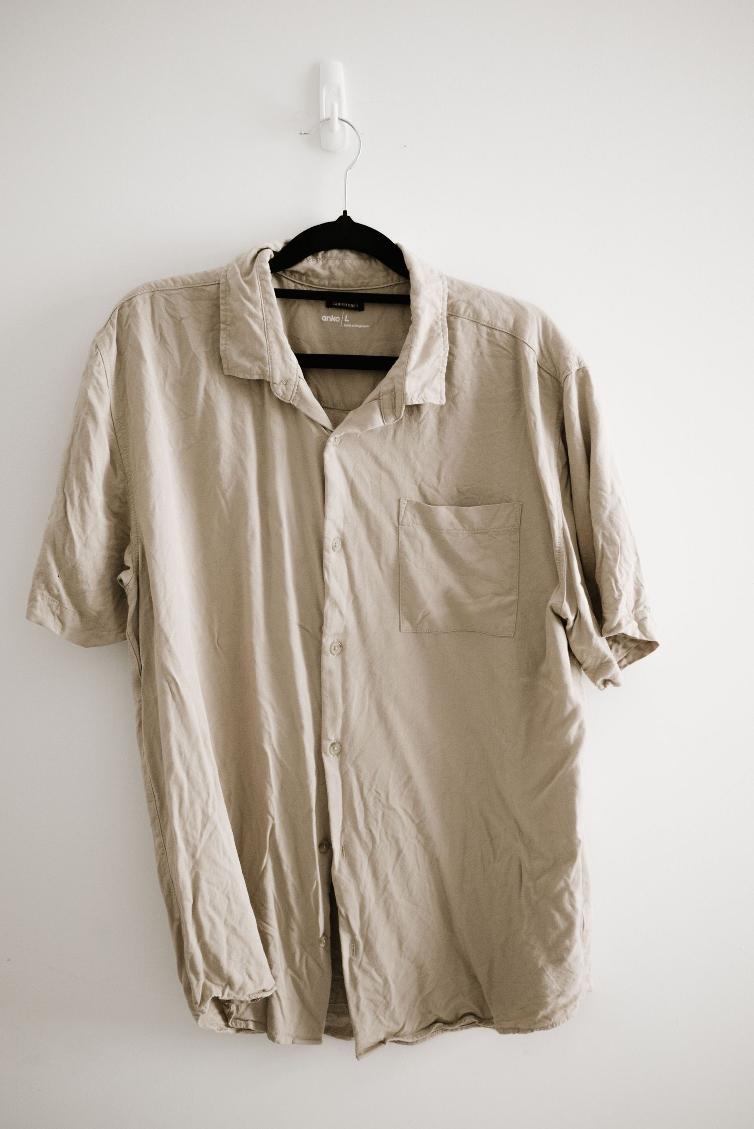 A light beige short-sleeve button-up shirt hanging on a black hanger.