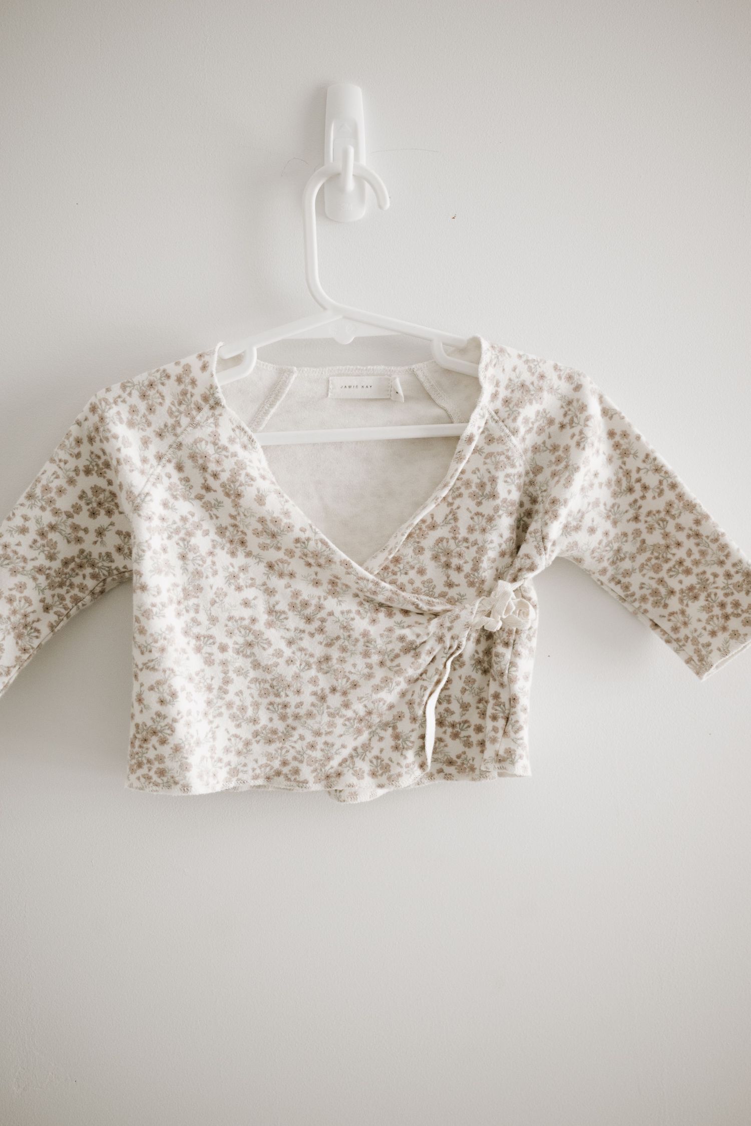 Small floral print wrap style baby cardigan in cream color hanging on white hanger.