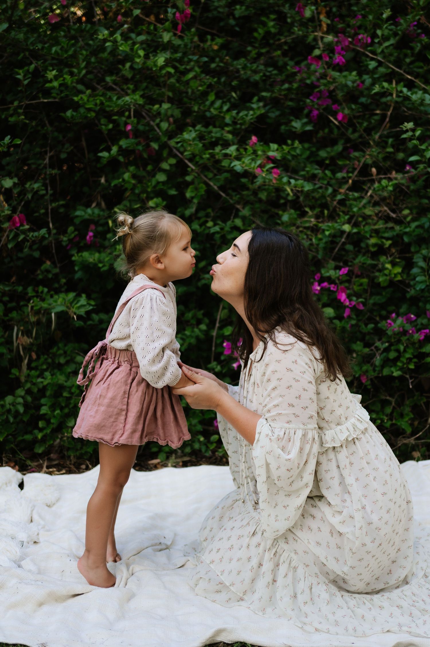 A sweet moment captured between parent and child in matching outfits against a backdrop of flowering bushes.