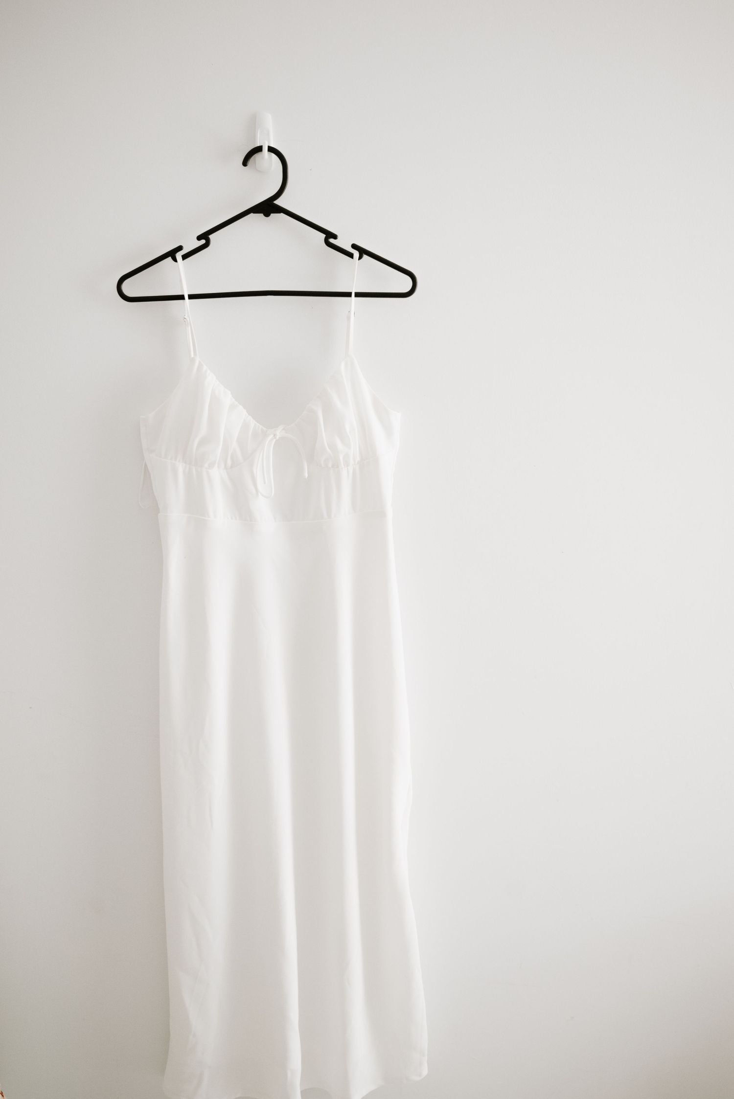 White silk slip dress with spaghetti straps hanging on black plastic hanger.