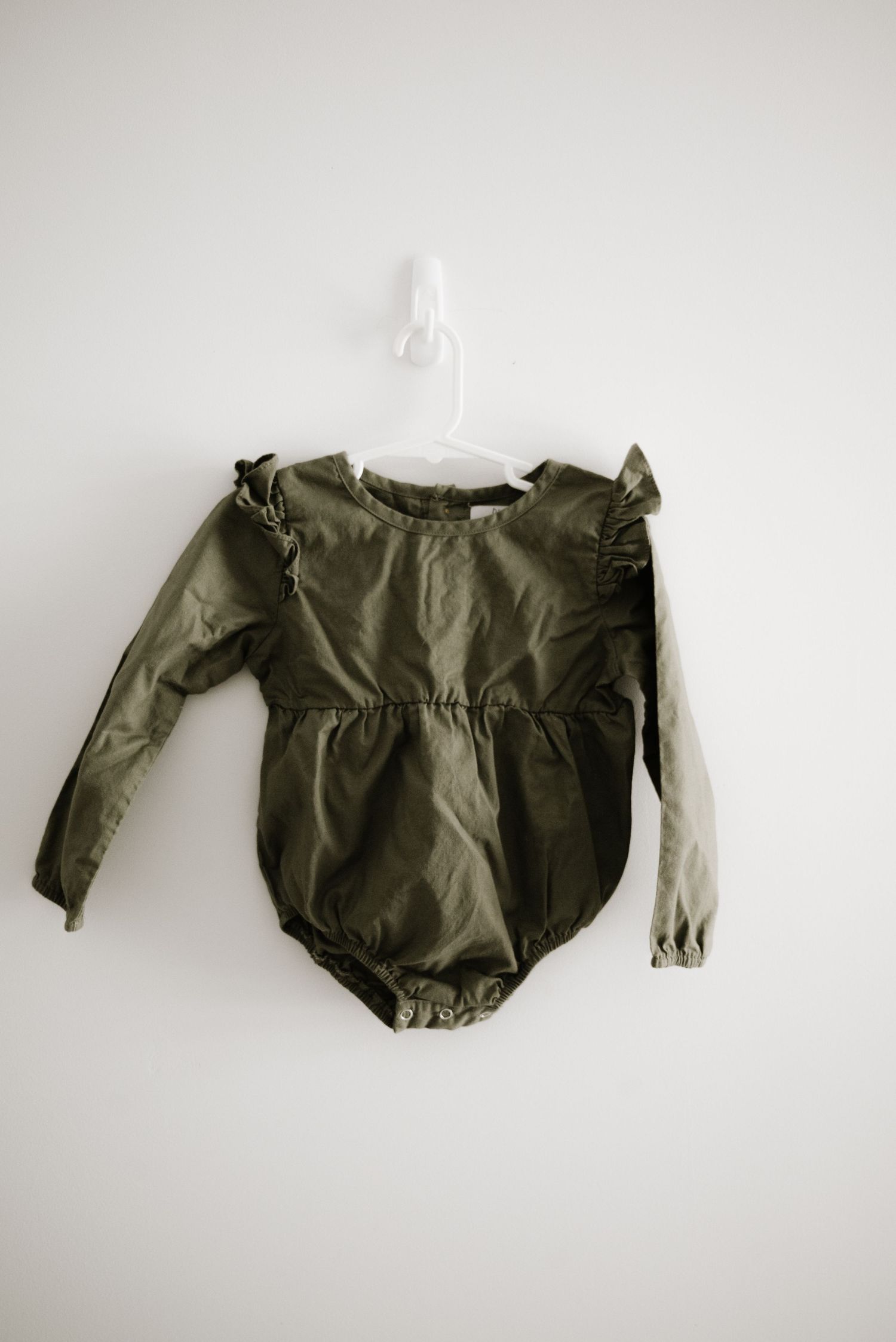 Olive green long-sleeve baby romper with ruffle details hanging on white hanger.