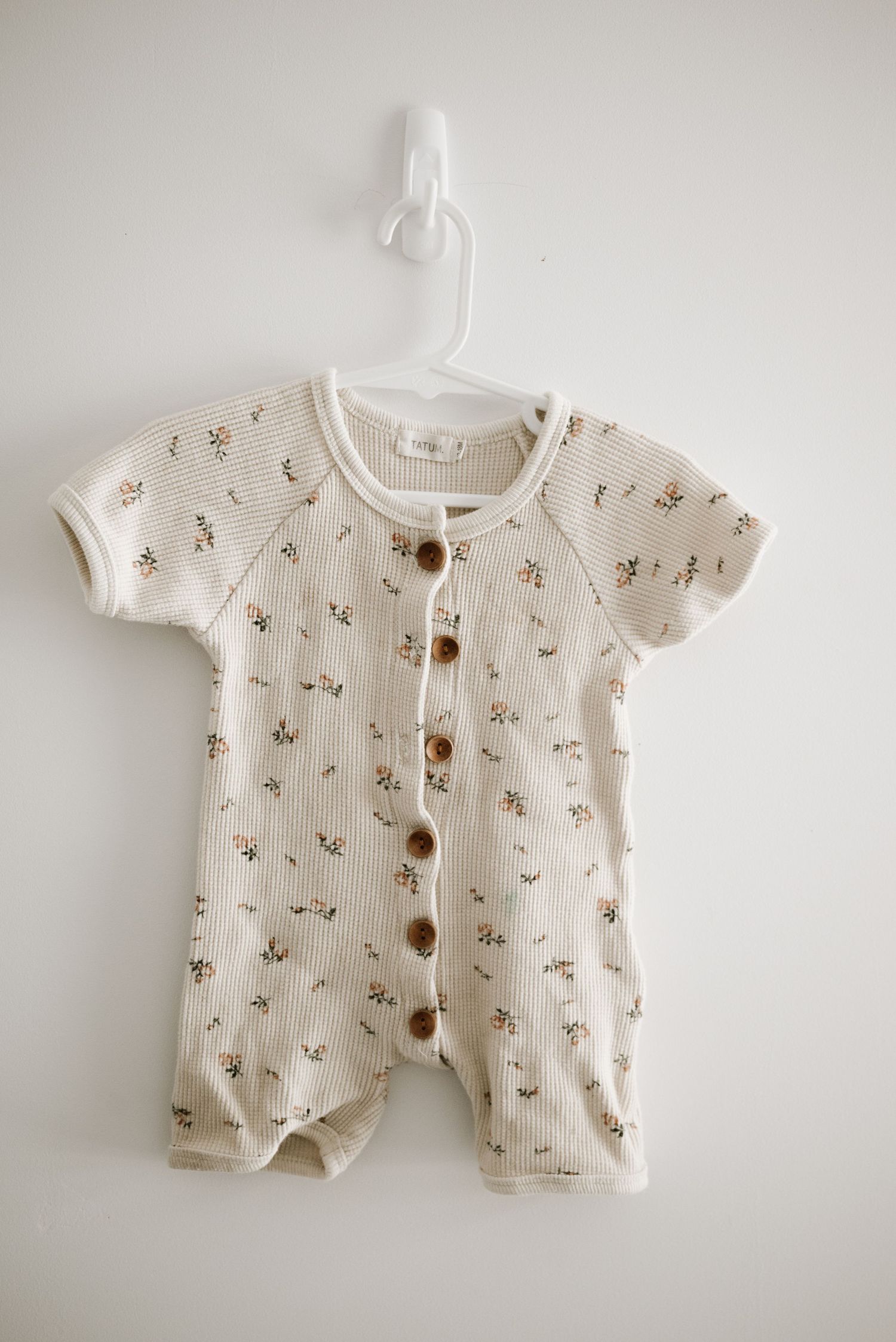 A cream colored baby romper with small floral print and wooden buttons down the front.