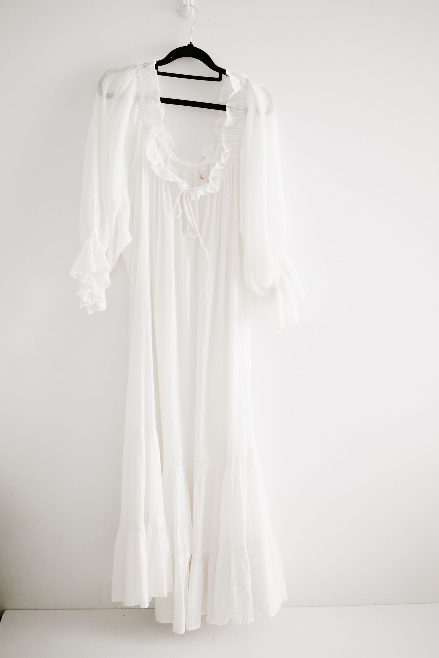 A flowing white cotton nightgown with long sleeves and lace trim displayed on a hanger.