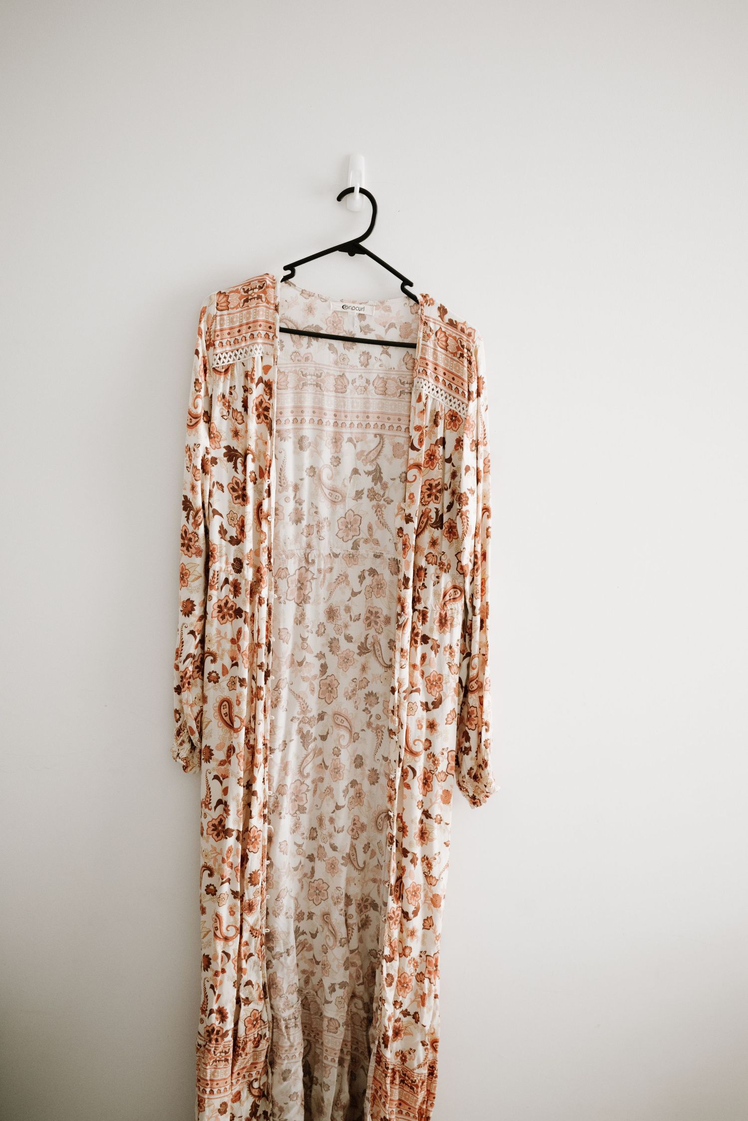 Floral print peach-colored long cardigan with delicate pattern hanging on black hanger.