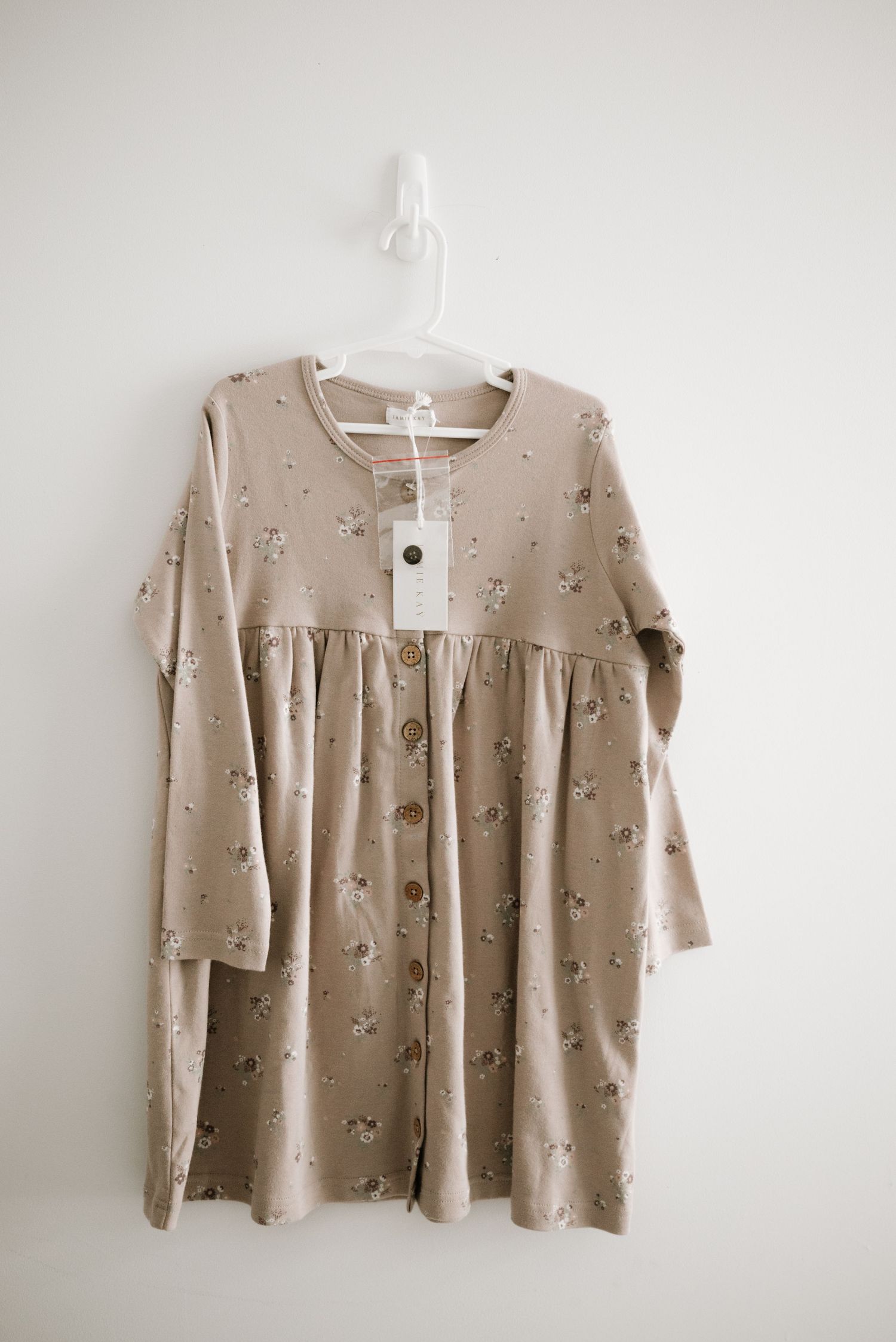 Tan floral print dress with long sleeves and empire waist hanging on white hanger.