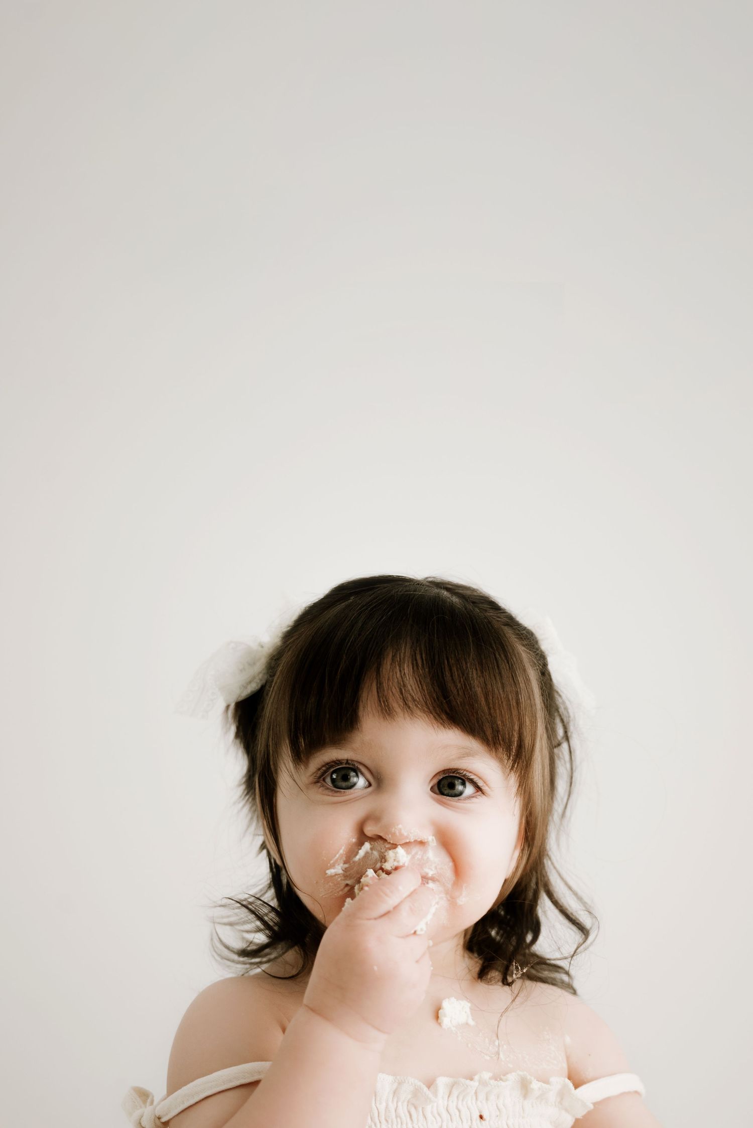 Sweet toddler with a messy face wearing a light-colored garment against a white background.
