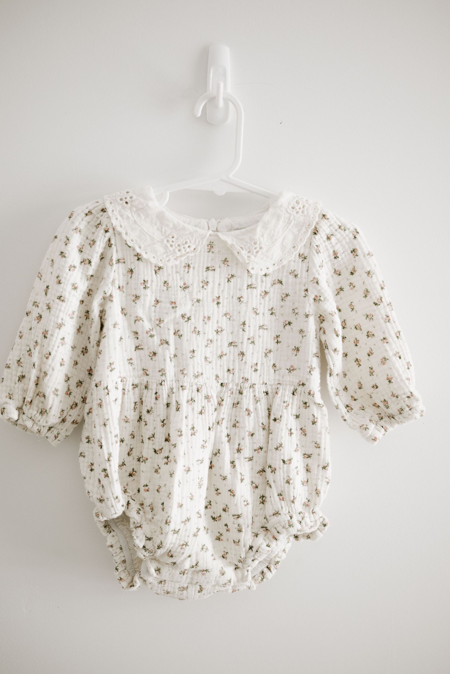 A white floral print baby romper with peter pan collar and puff sleeves.