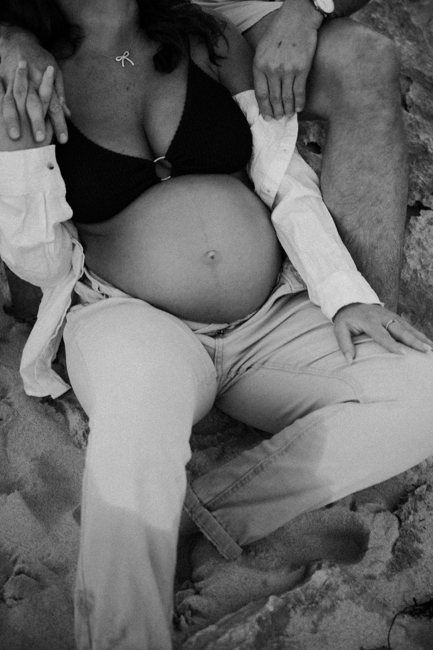 Black and white photo of a pregnant belly exposed through unbuttoned white shirt while resting.