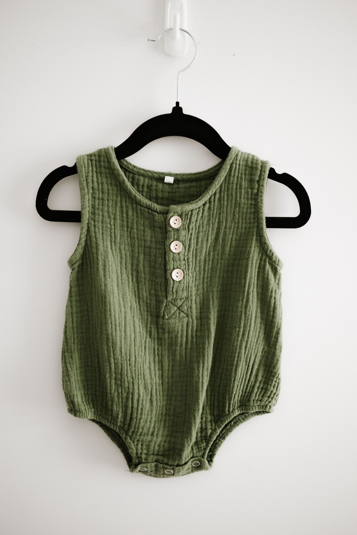 Sage green muslin baby romper with button front detail hanging on black hanger.