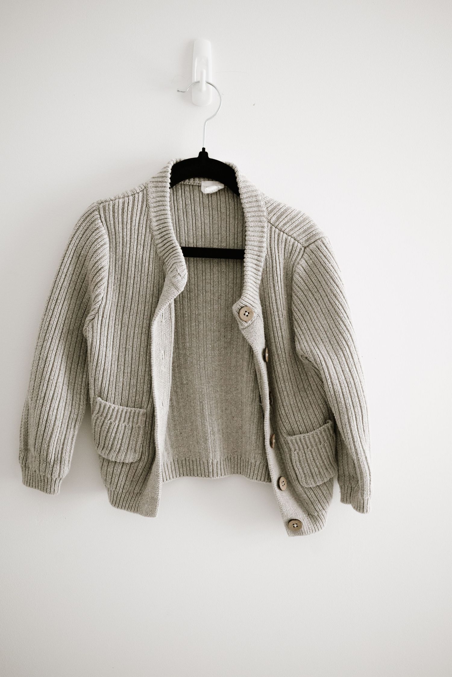 Gray knit cardigan sweater with pockets and buttons hanging on black hanger.