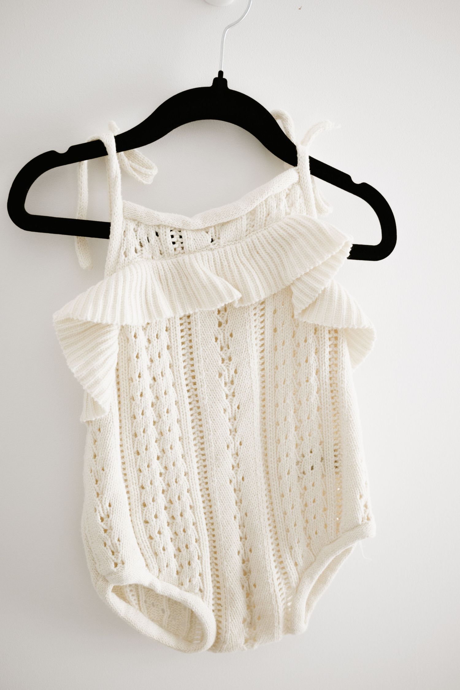 Vintage-style white crochet lace bodysuit with ruffled neckline displayed on black hanger.