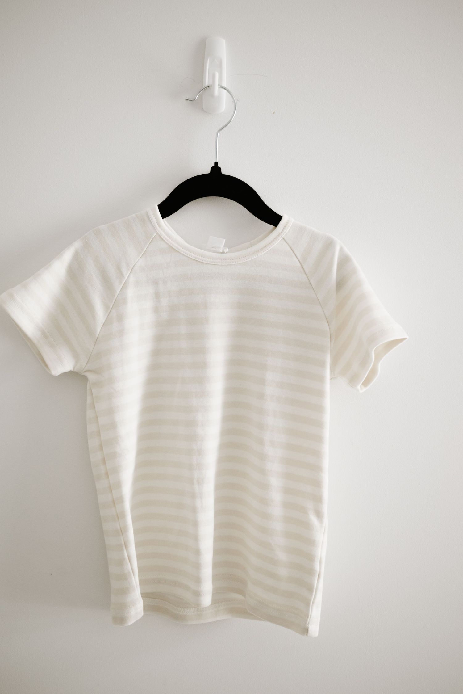 White striped short sleeve t-shirt hanging on black hanger against light wall.