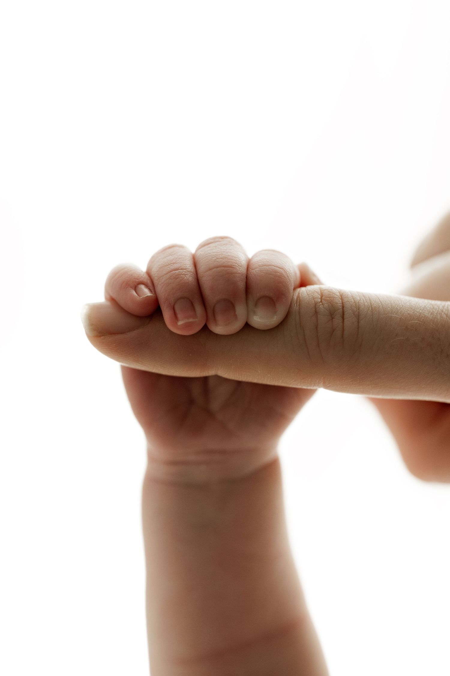 Close-up of tiny newborn hand grasping adult finger in tender moment.