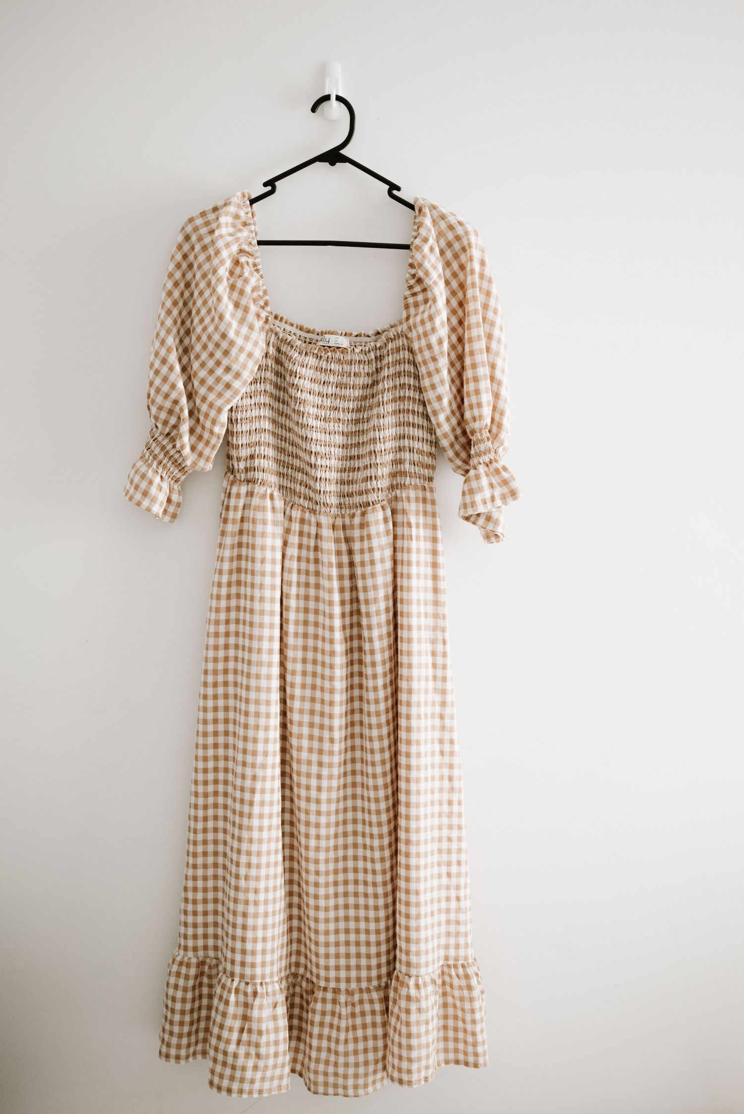 A beige gingham maxi dress with ruched bodice and puffy sleeves on a black hanger.