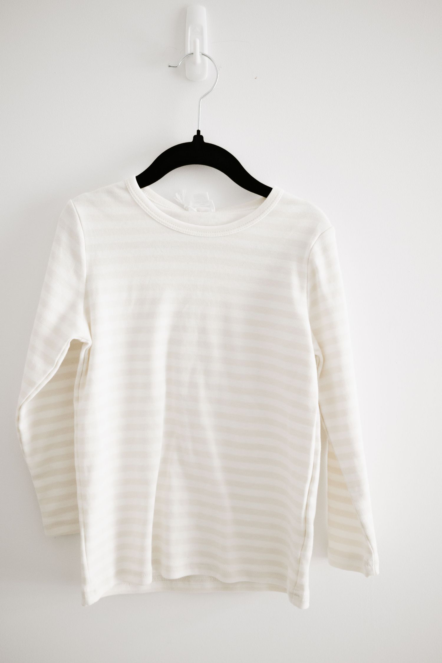 White striped long sleeve t-shirt hanging on black hanger against white wall.