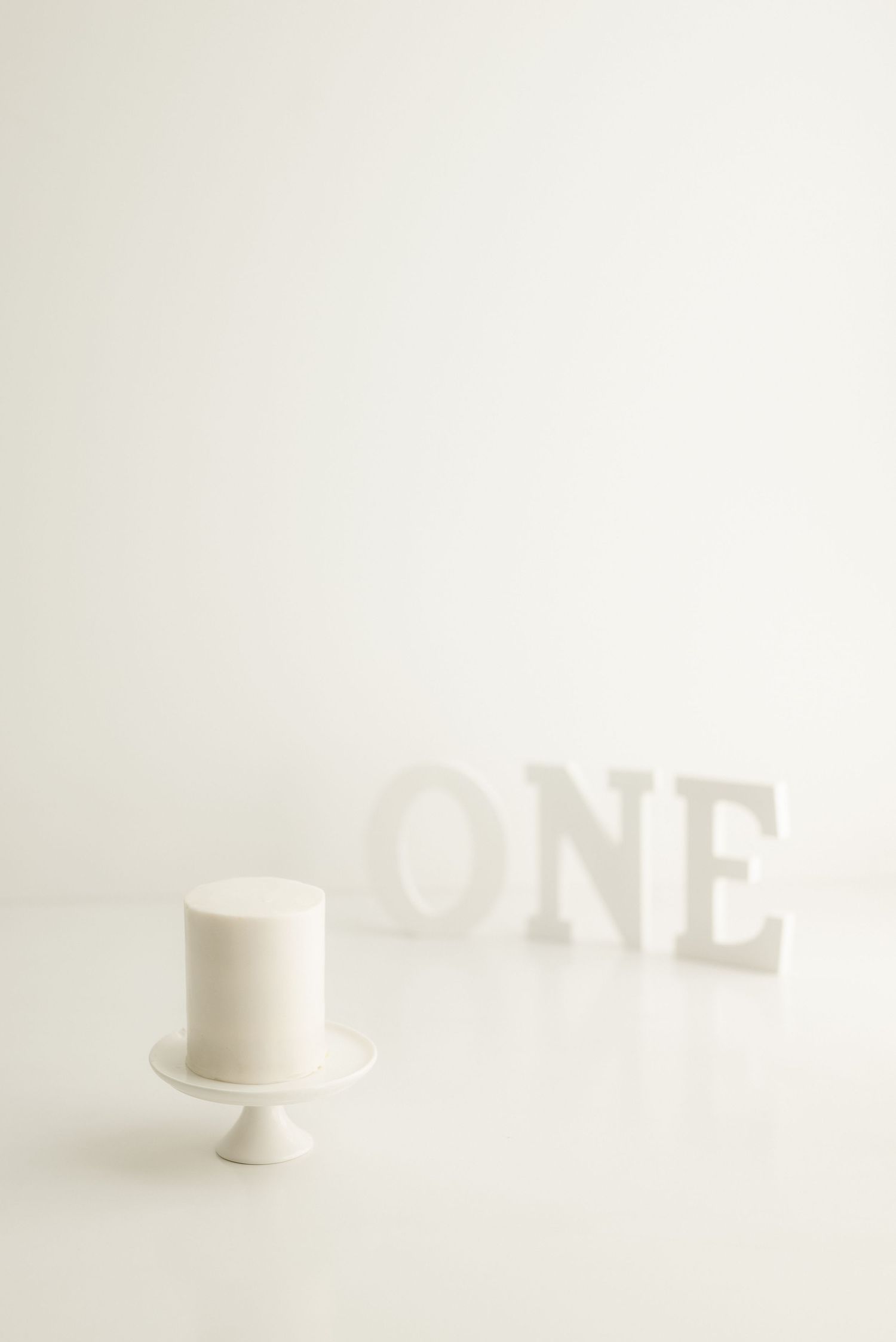 White cake on pedestal stand with 'ONE' text shadow in background.