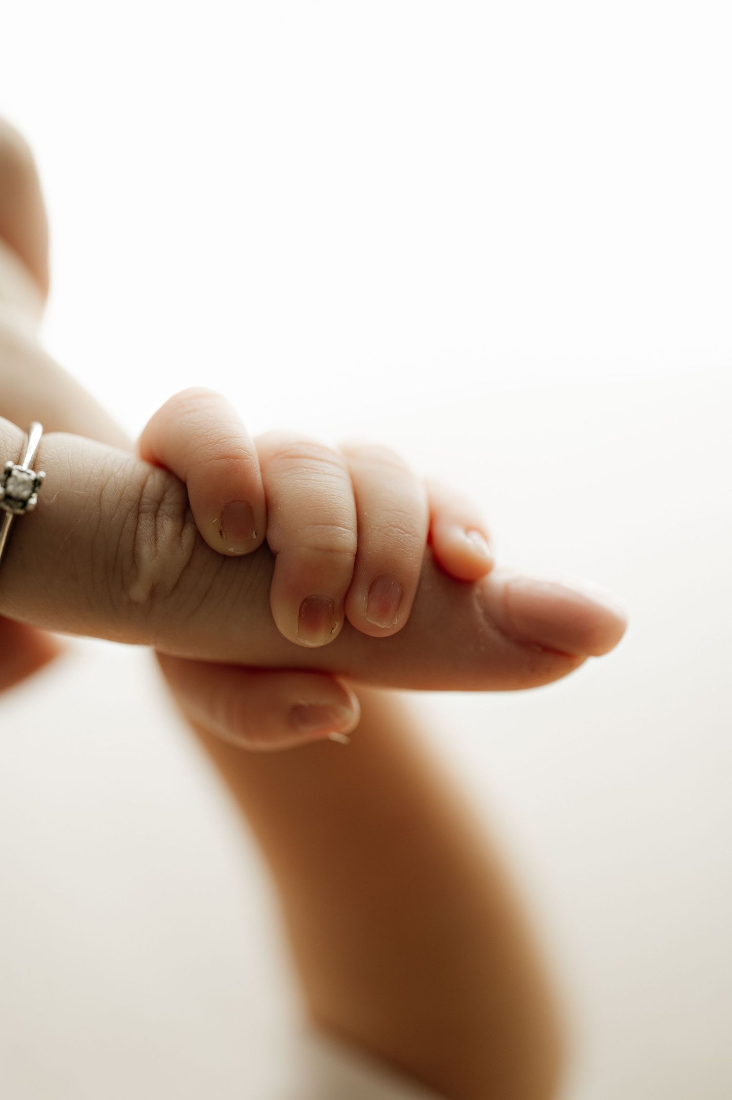 Tiny newborn hand grasping adult finger in soft natural light.