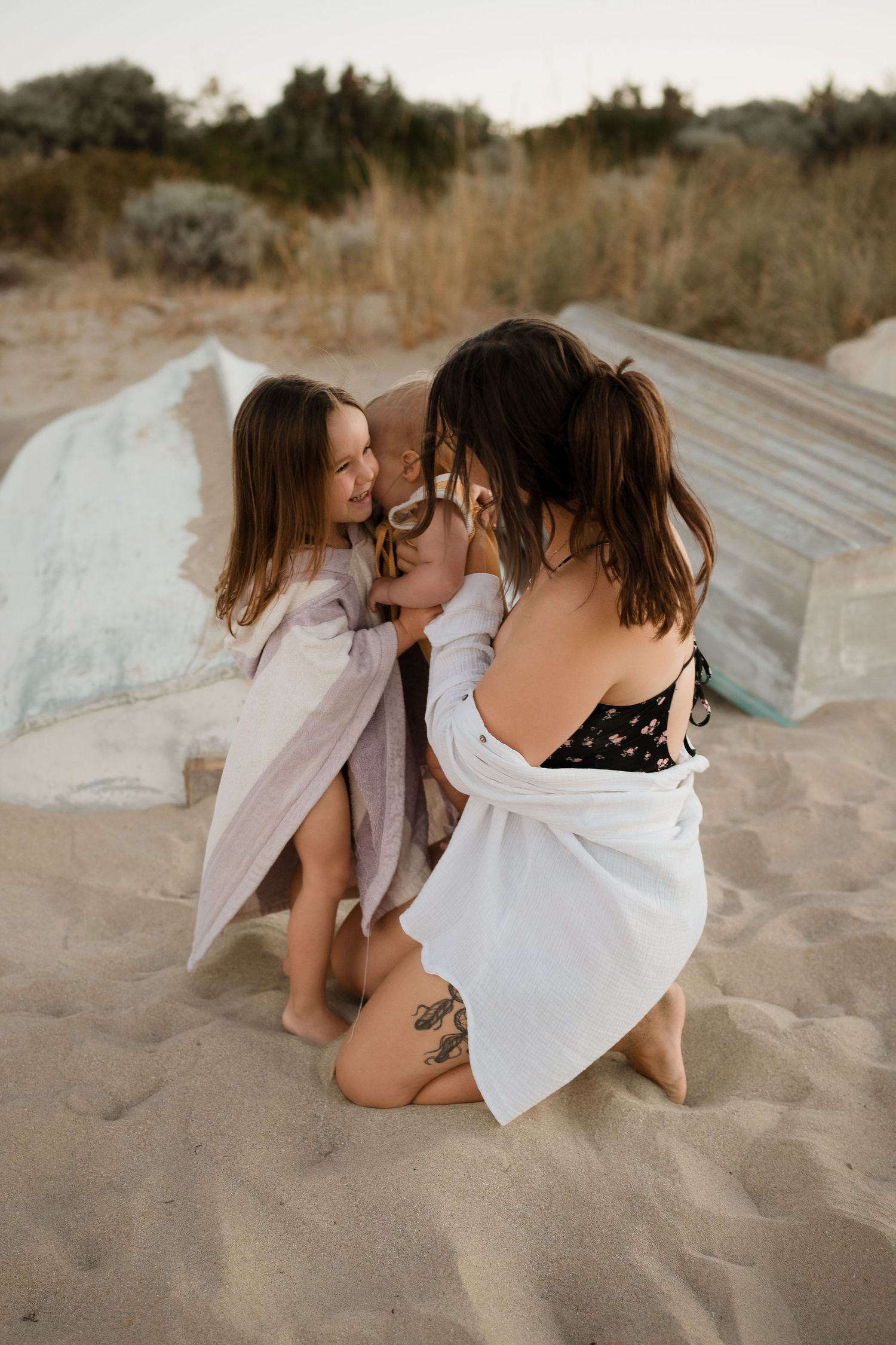 Intimate family moment on sandy beach with white blankets at sunset.