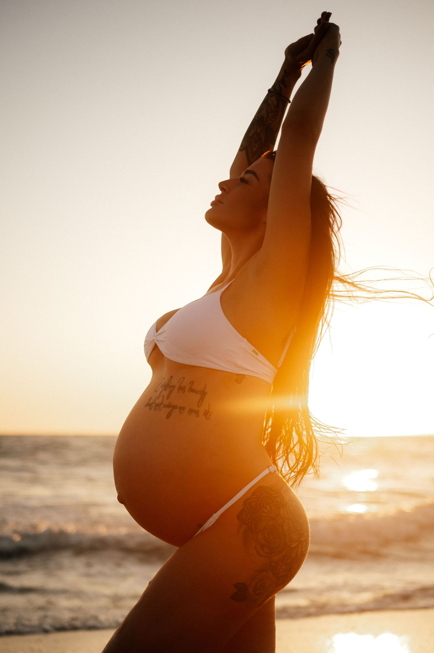 Silhouette of pregnant woman stretching on beach at sunset.