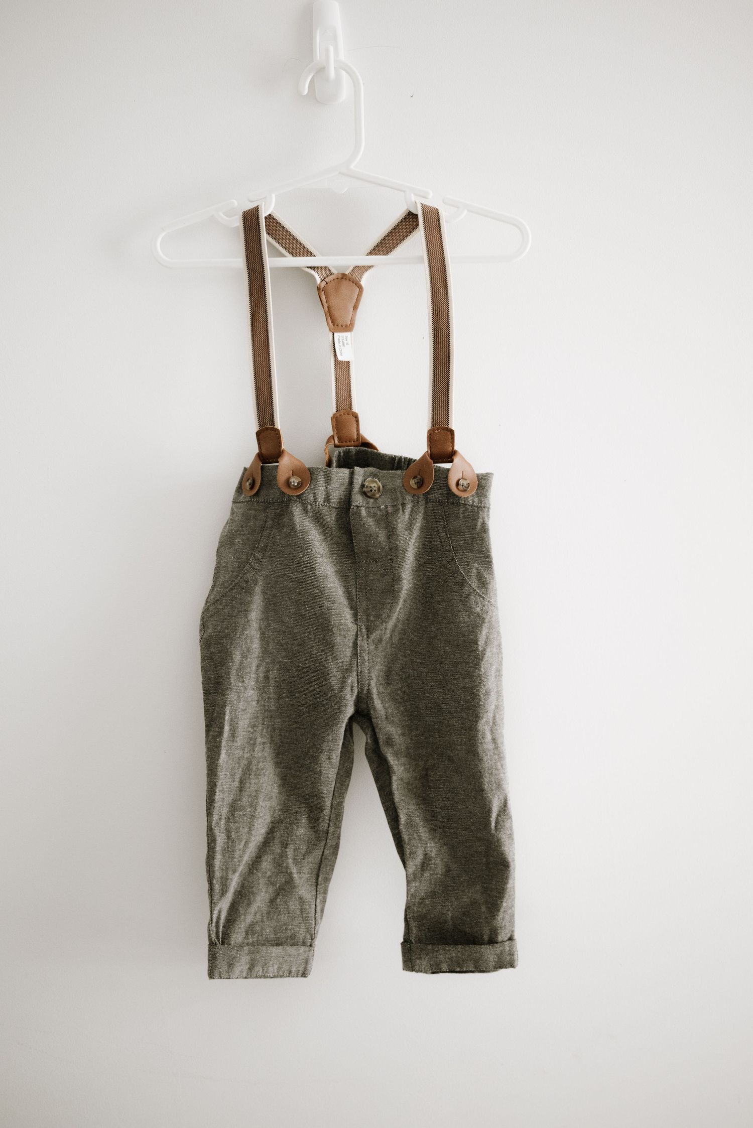 Gray pants with brown leather suspenders hanging on white plastic hanger.