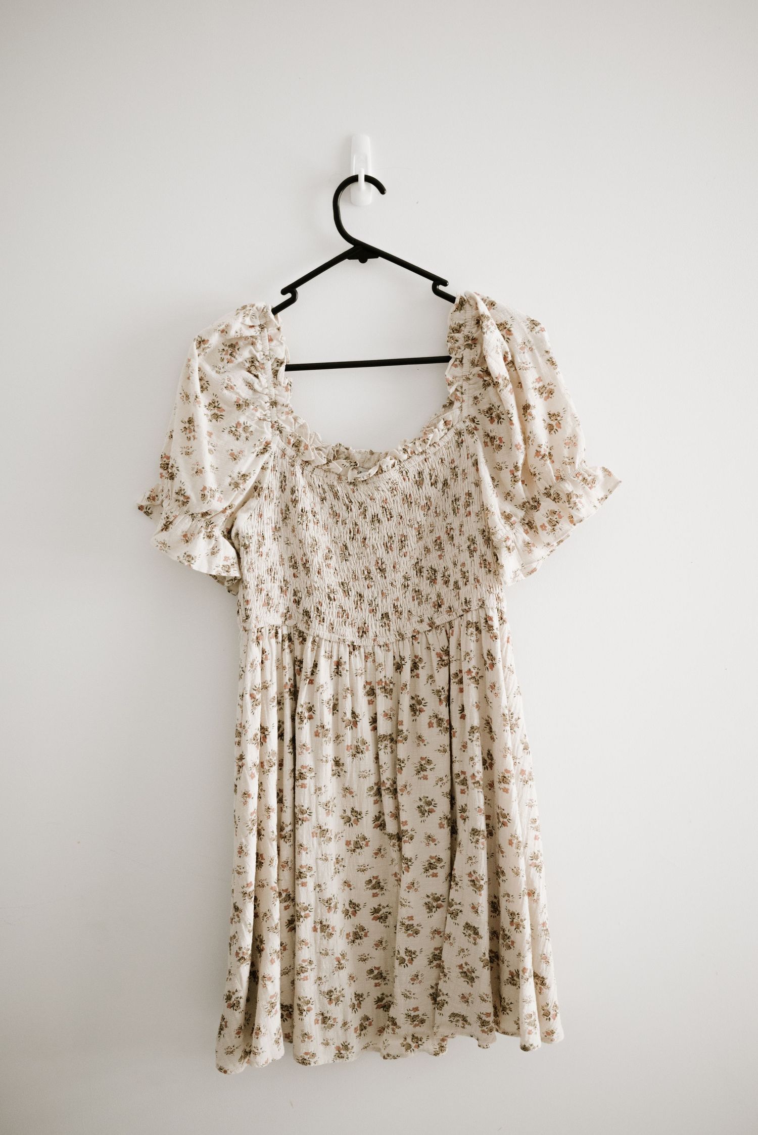 Cream-colored floral dress with smocked bodice and puff sleeves on black hanger.