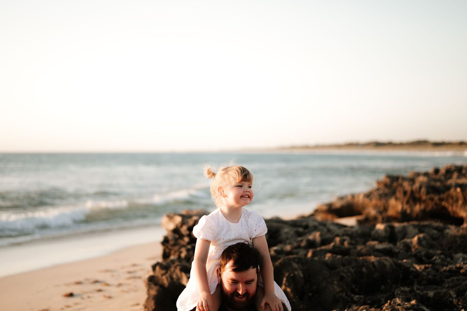 A sunset beach portrait captures playful moments against rocky coastal scenery.