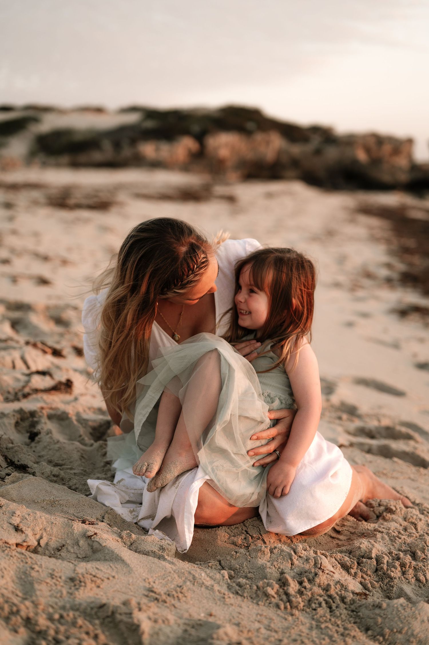 Intimate beach portrait showing tender moment between two people in white dresses at sunset.