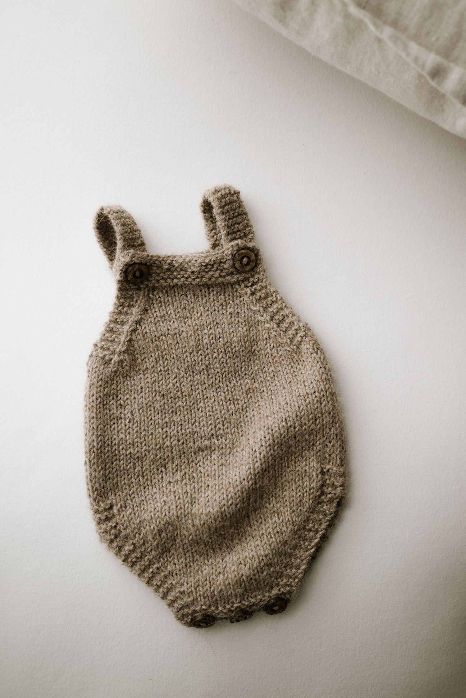 Hand-knitted taupe baby romper photographed on white background.