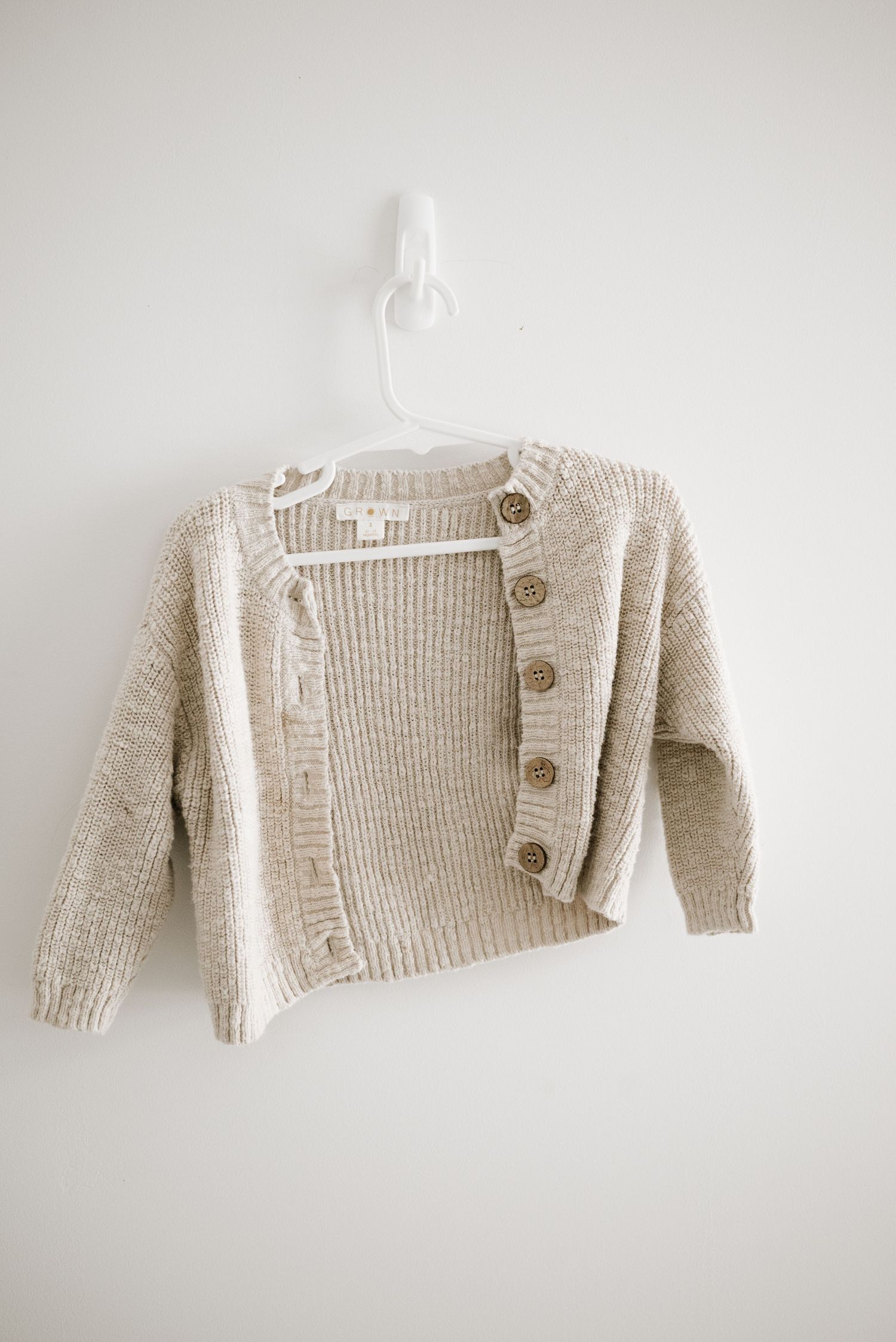 Cream colored knit cardigan sweater with large buttons hanging on white hanger.