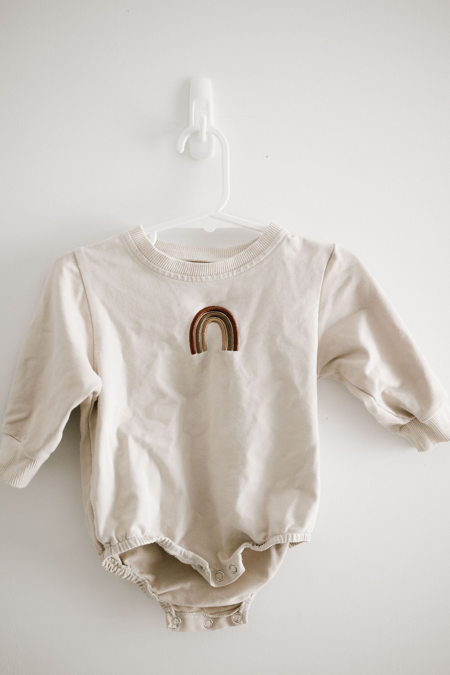 A cream colored baby onesie featuring a brown rainbow design on the front.