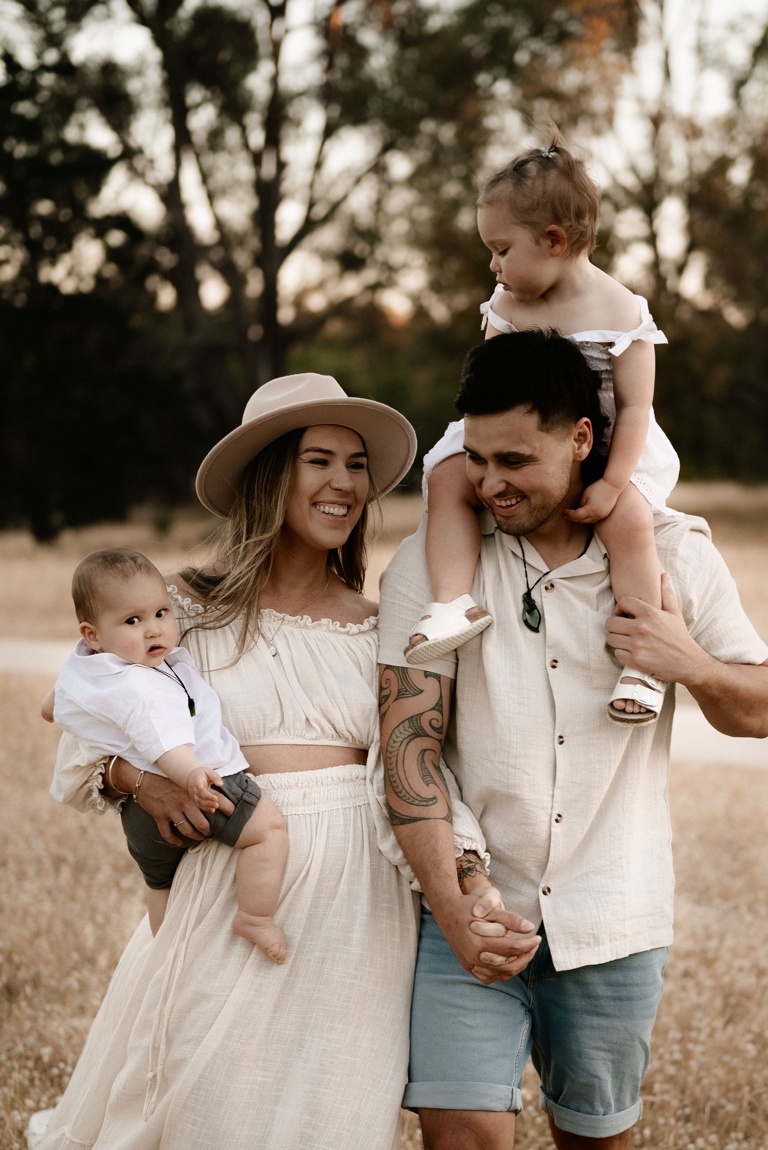 Family in neutral outfits posing together in golden field at sunset.
