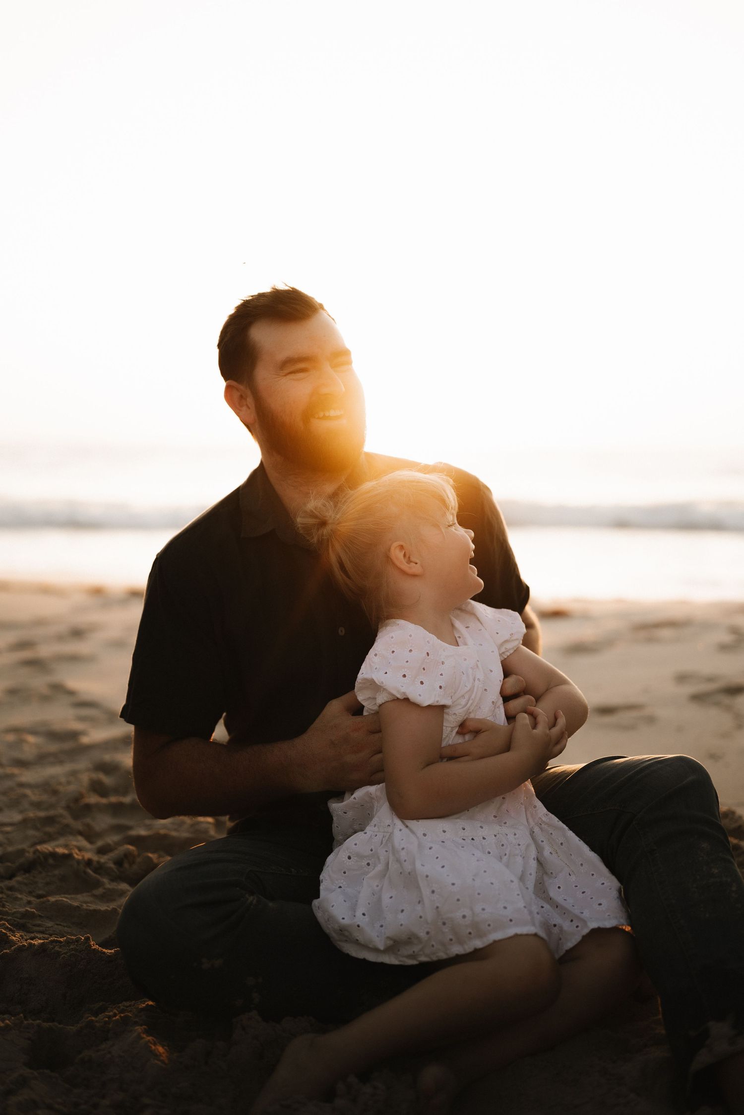 Warm sunset light illuminates tender moments between family members on a sandy beach.