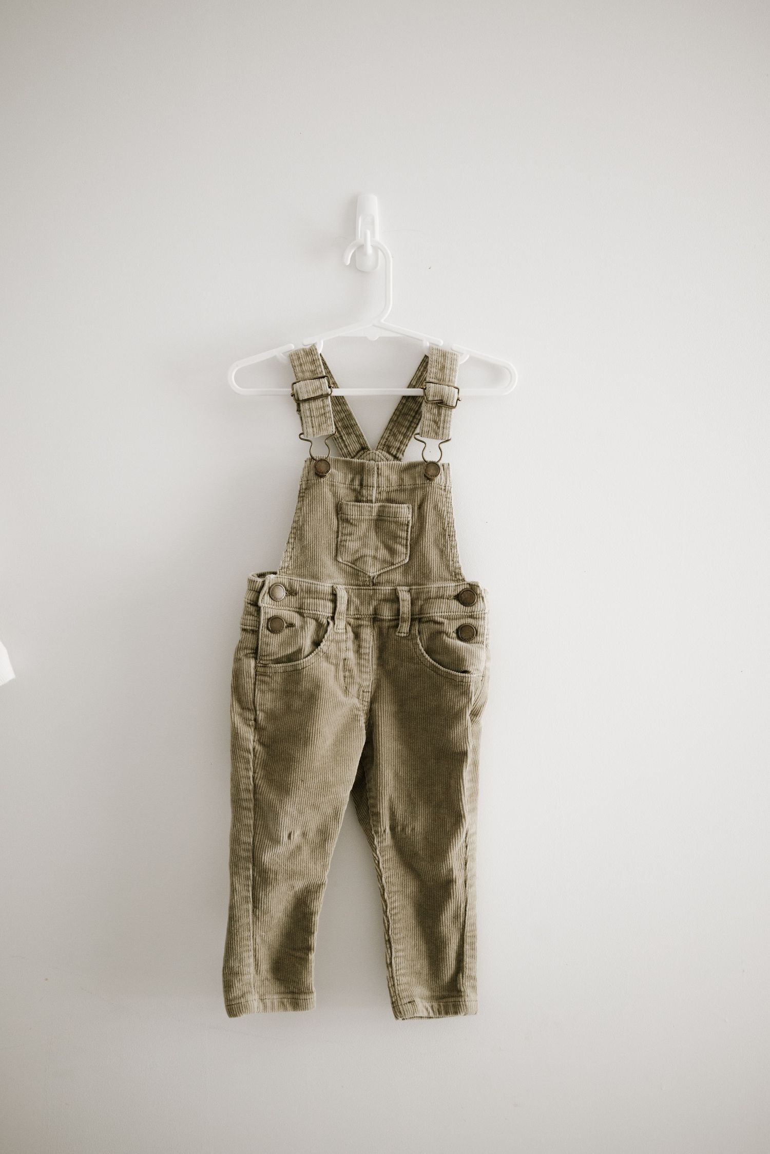 Khaki corduroy baby overalls with adjustable straps hanging on white hanger.