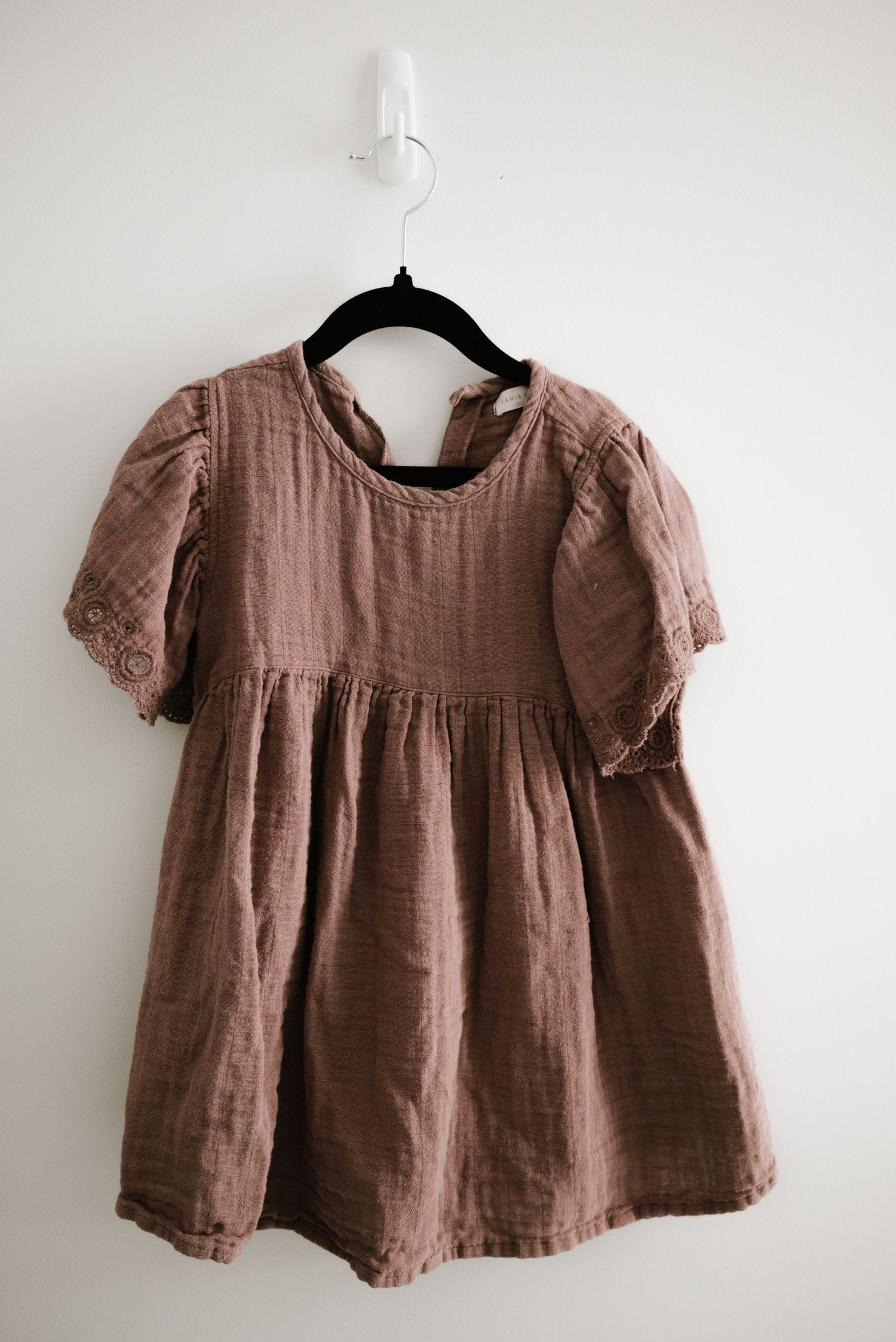 Dusty rose linen dress with puffed sleeves and empire waist hanging on black hanger.