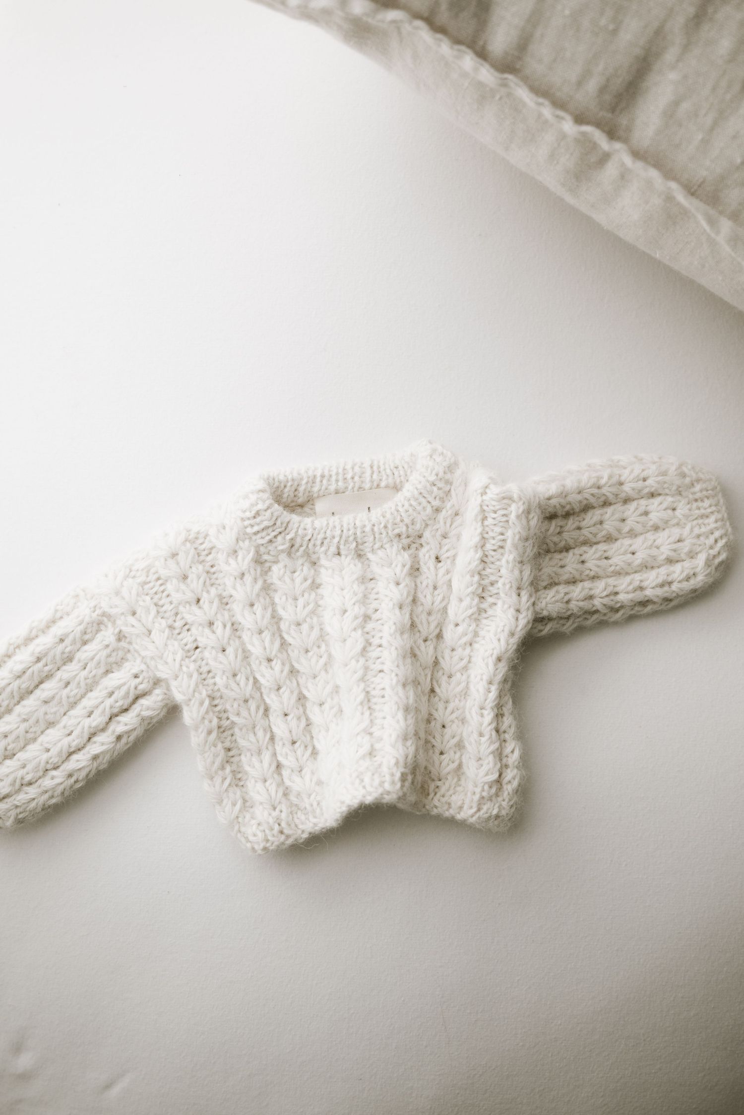 Cream cable knit baby sweater laid flat on white surface.