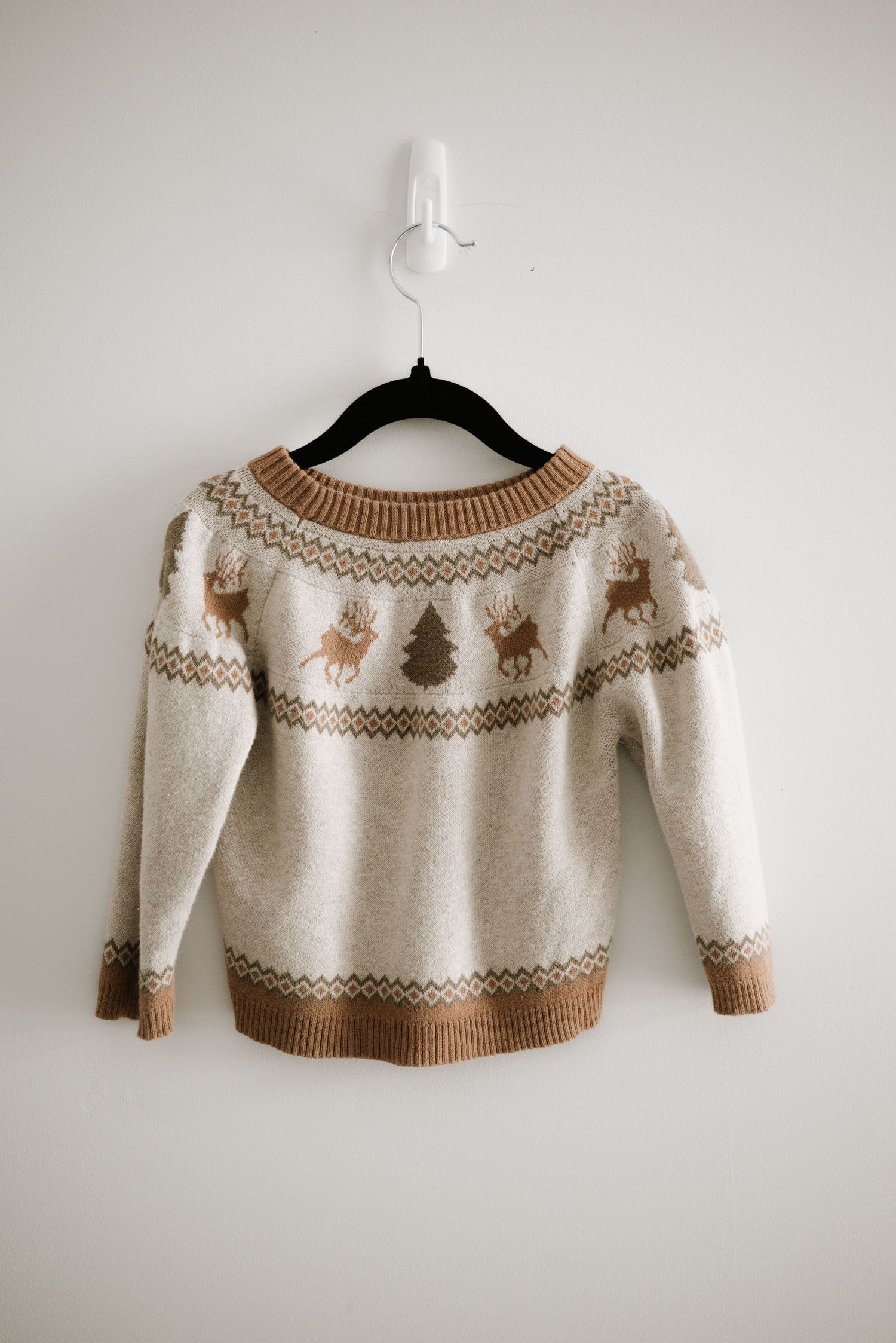 Cream and tan knit sweater with winter pattern design hanging on black hanger.