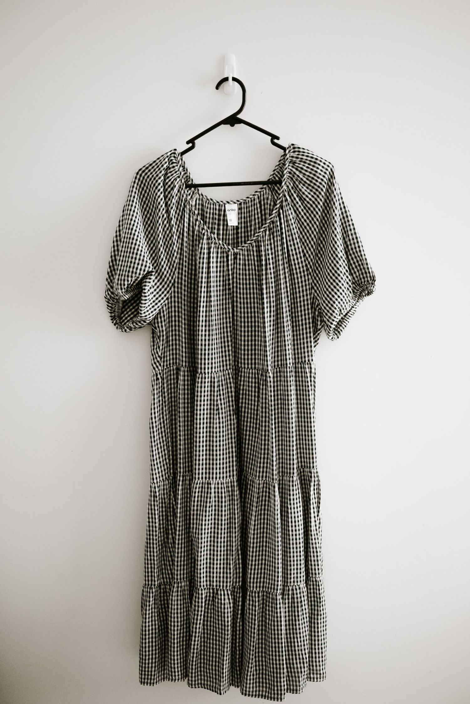 Black and white gingham midi dress with puff sleeves and tiered skirt on hanger.
