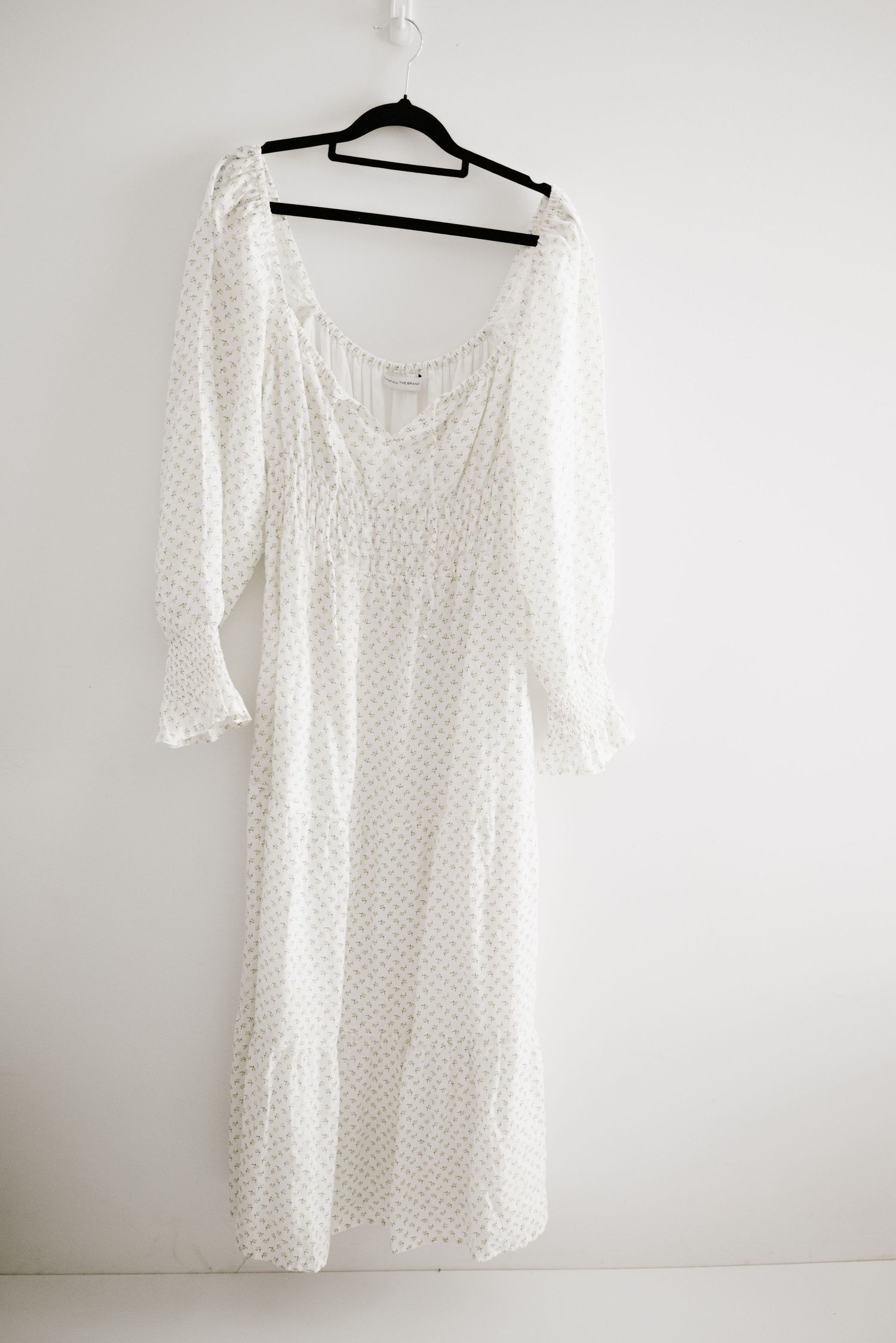A white cotton dress with delicate dot pattern and long sleeves displayed on a hanger.