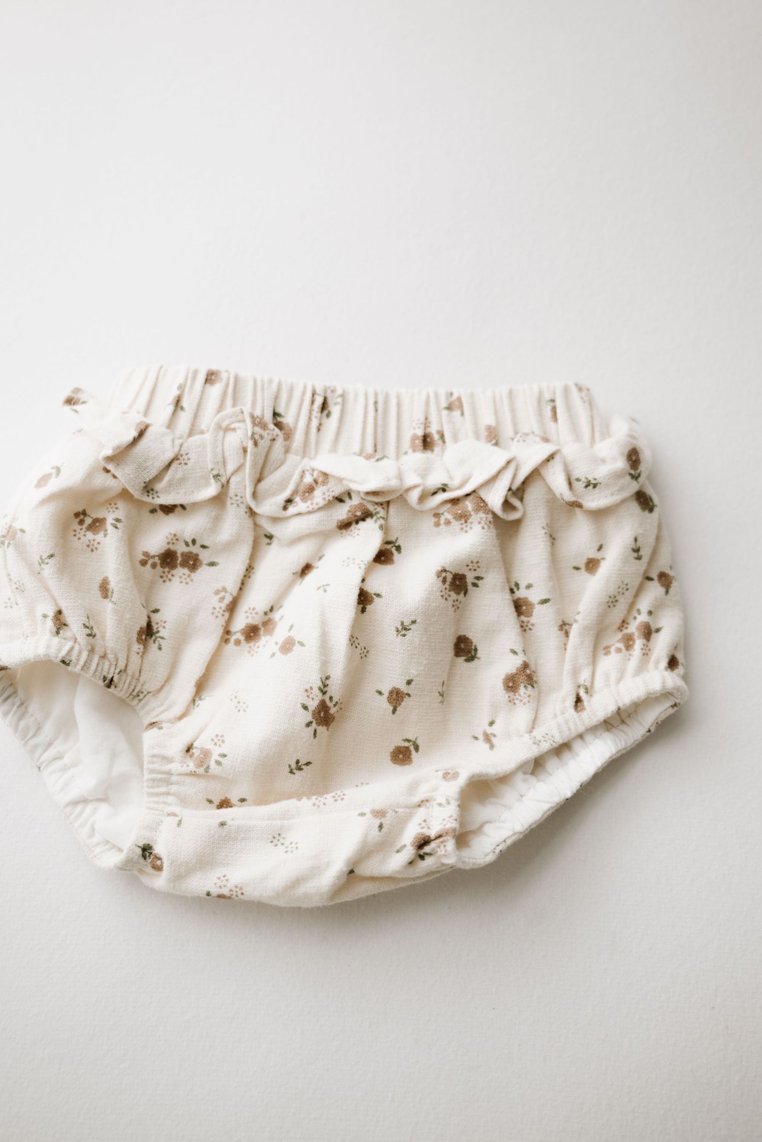 White cotton baby bloomers with delicate floral print pattern.